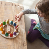 Mädchen spielt mit dem Freies Spiel: Perpetual Calendar, bestehend aus bunten Holzfiguren, Tageswürfeln und einem Jahreskreis, handgefertigt aus nachhaltig produziertem Holz.