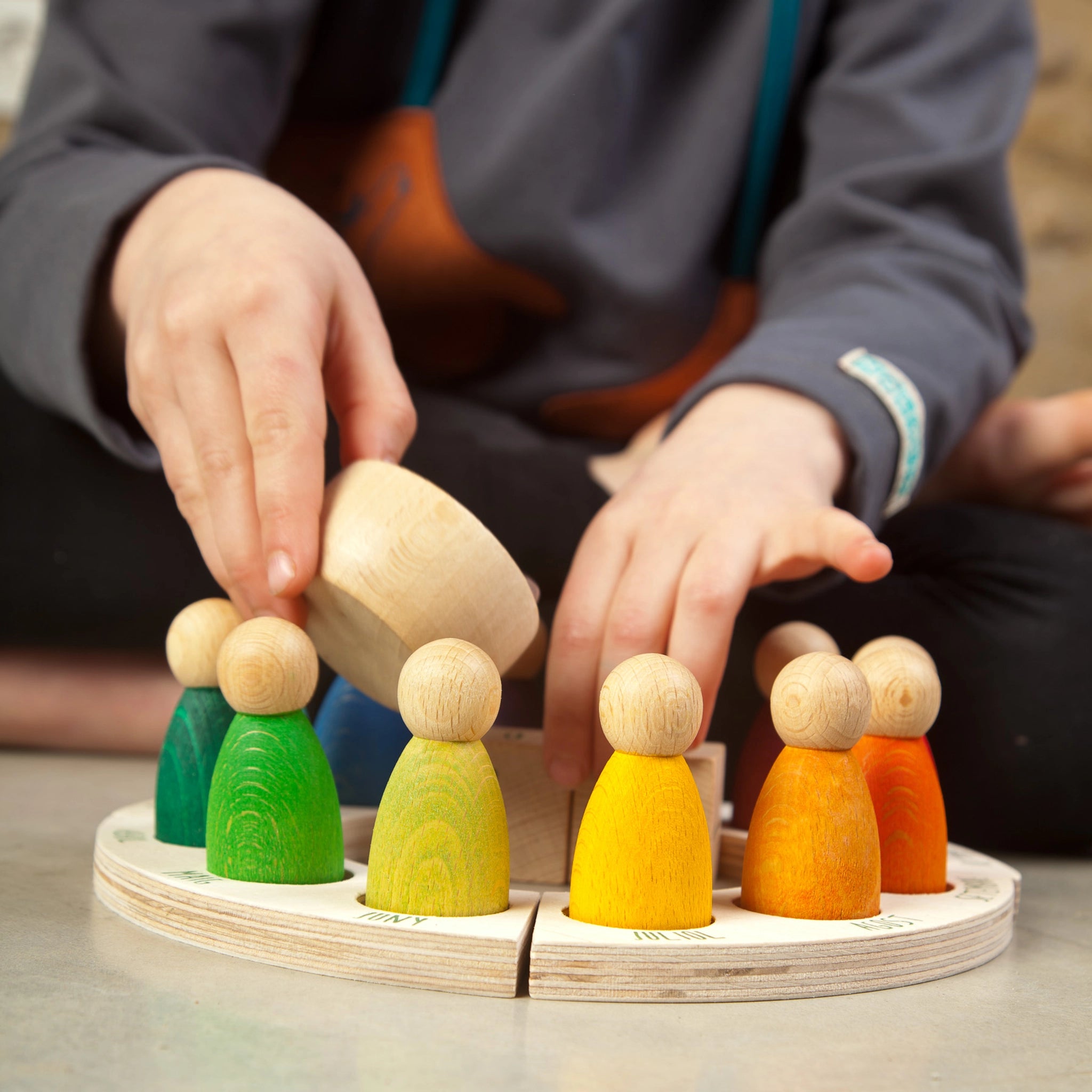 Freies Spiel: Perpetual Calendar zeigt eine Person, die mit handgefertigten Holzfiguren, darunter 12 Nins-Figuren, ein Schälchen und zwei Tageswürfel, interagiert. Perfekt zur Förderung des Zeitverständnisses.