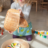 Freies Spiel: Sticks – Ein Mädchen hält einen Korb und eine Schale mit handgefertigten, nachhaltigen Holzfiguren, ideal für kreatives Kinderspiel. Perfekt für moderne, umweltbewusste Familien.