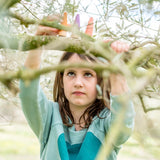 Mädchen hält Freies Spiel: Sticks, handgefertigt aus nachhaltig geforstetem Holz. Set aus 18 bunten Figuren, ideal fürs freie Spiel. Nachhaltiges Design vereint Ästhetik und Spielspaß, passend zu KLICKKLACKs Ethos.