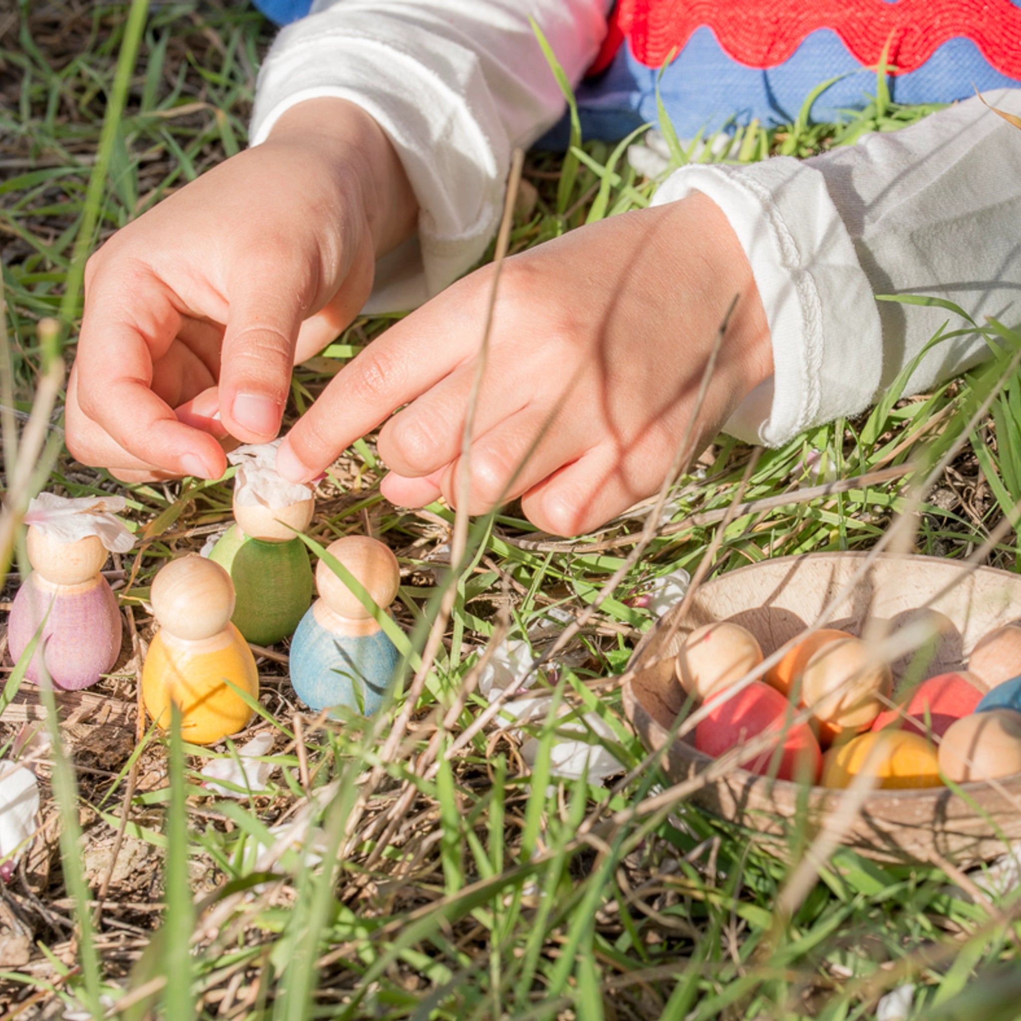 Freies Spiel: Baby Nins – Ein Kind spielt mit handgefertigten, bunten Holzfiguren. Die 6 Baby Nins-Figuren sind in einer Kokosnussschale präsentiert, ideal für kreatives Spielen.