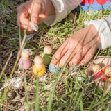 Freies Spiel: Baby Nins, sechs handgefertigte Holzfiguren in einer Kokosnussschale, gehalten von einer Hand. Ideal für kreatives Kinderspiel, nachhaltig produziert.