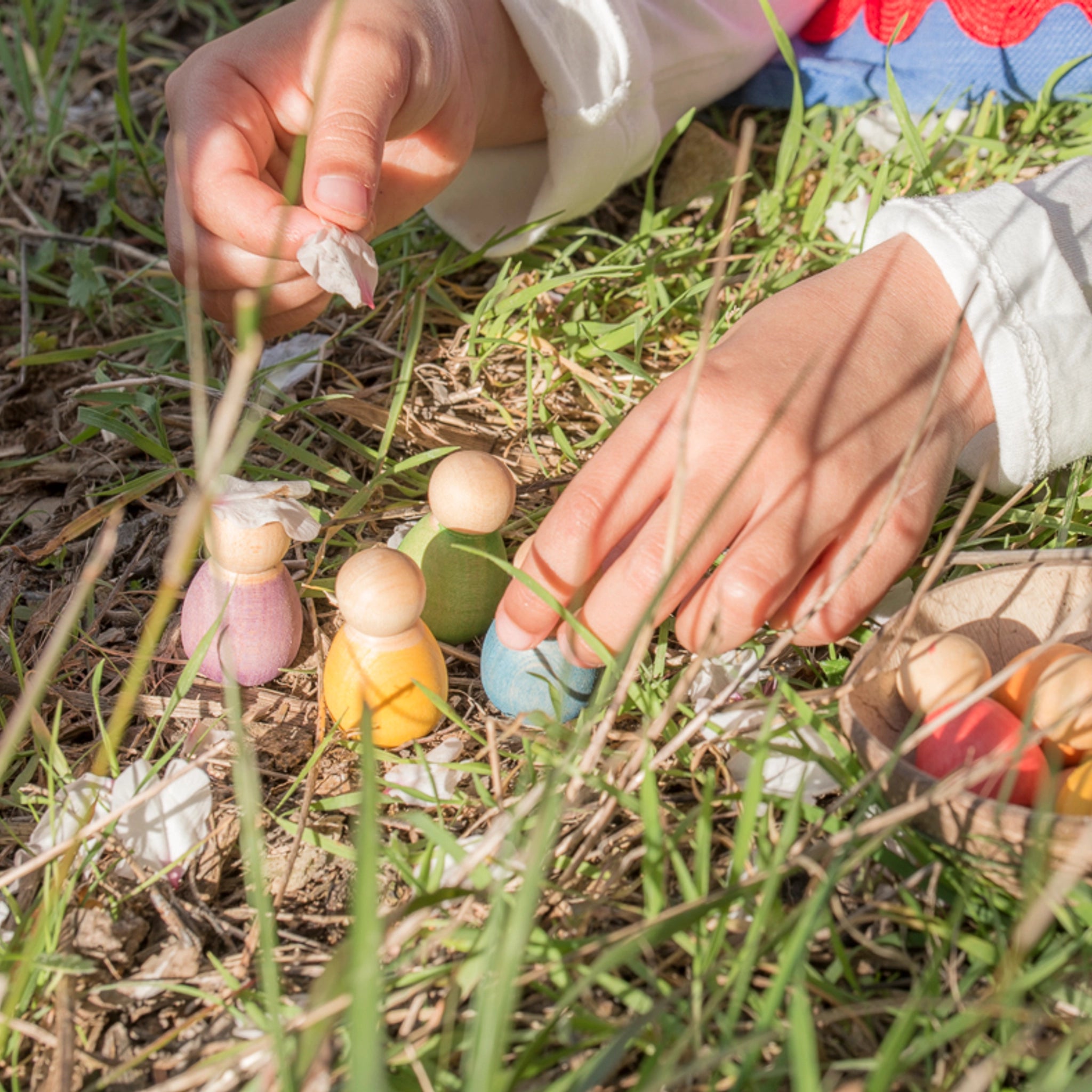 Freies Spiel: Baby Nins, sechs handgefertigte Holzfiguren in einer Kokosnussschale, gehalten von einer Hand. Ideal für kreatives Kinderspiel, nachhaltig produziert.