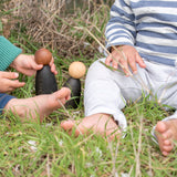 Freies Spiel: Dark Adult Nins, zwei handgefertigte Figuren aus nachhaltig geforstetem Holz, ideal für kindgerechtes freies Spiel, im Gras spielend. Perfekt kombinierbar mit klassischen Grapat Nins.