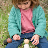 Freies Spiel: Dark Adult Nins aus dunklem Holz, handgefertigt in Spanien, ideal für freies Spiel. Abgebildet neben einem Mädchen im Gras, verkörpert nachhaltige und kreative Spielmöglichkeiten.