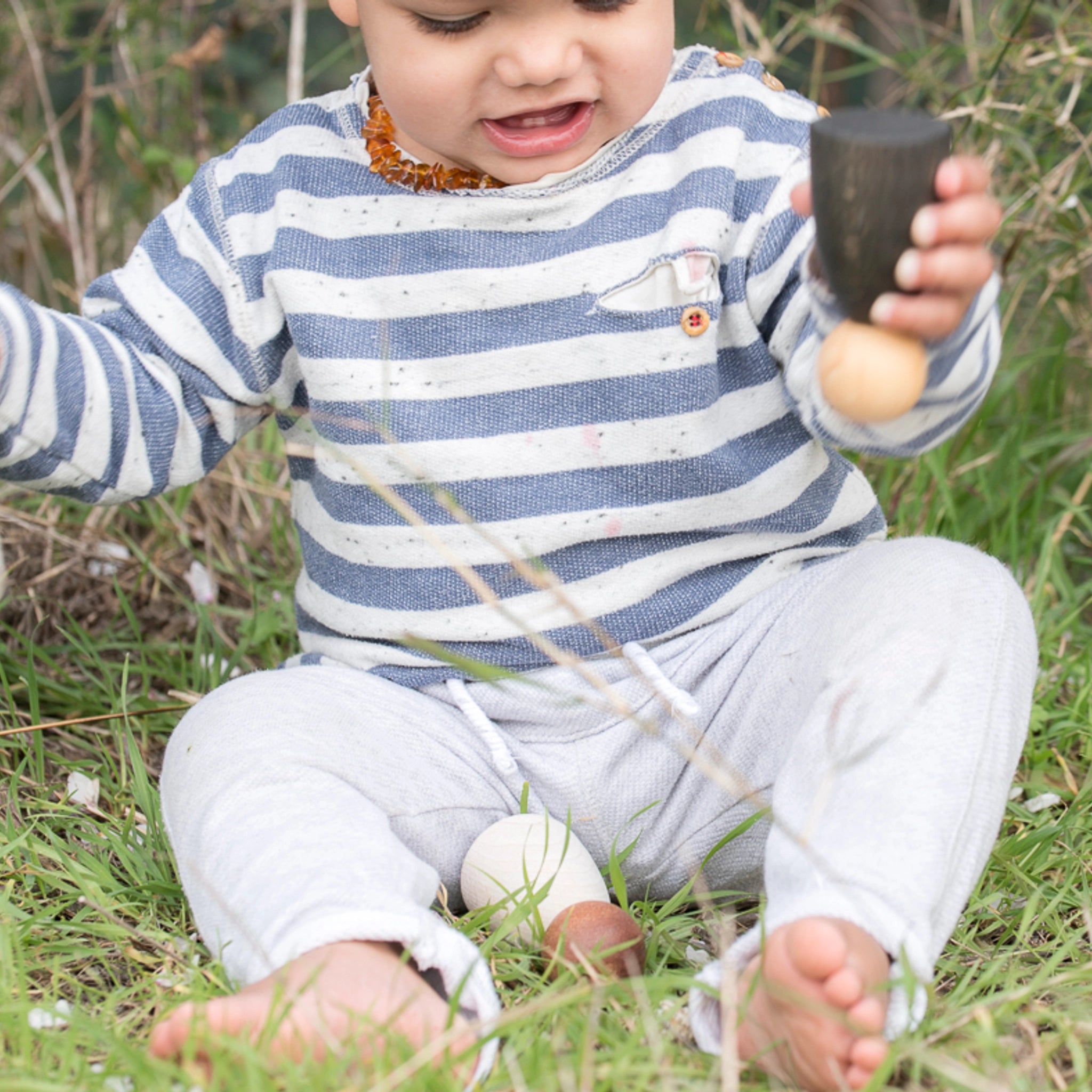 Freies Spiel: Adult Nins, zwei handgefertigte Erwachsenen-Figuren aus hellem Holz, gehalten von einem Baby im Gras. Ideal für kreatives, freies Spiel, passend zu Grapat Nins.