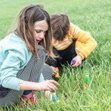 Zwei Kinder spielen im Gras mit dem Freies Spiel: Wizards Set. Das Set besteht aus nachhaltig hergestellten, handgefertigten Zauberer-Figuren in Regenbogenfarben, ideal für kreatives Spielen.