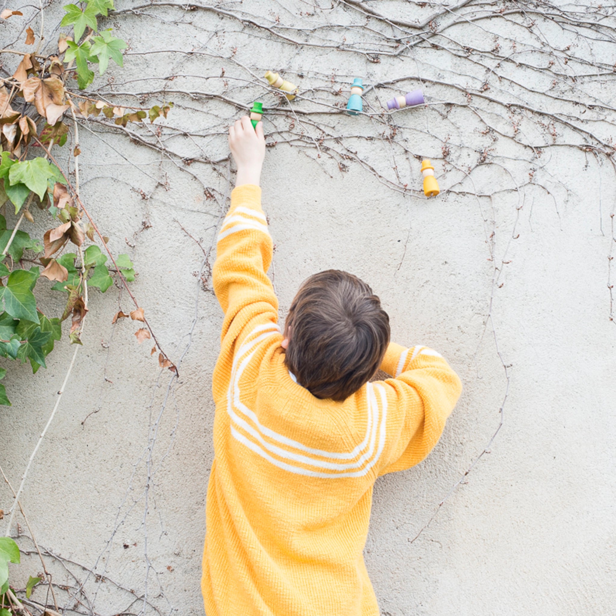 Freies Spiel: Wizards - Ein Kind malt spielerisch Ranken an eine Wand, während es in einem gelben Pullover steckt. Die handgefertigten, nachhaltigen Zauberer-Figuren fördern kreatives, freies Spiel.