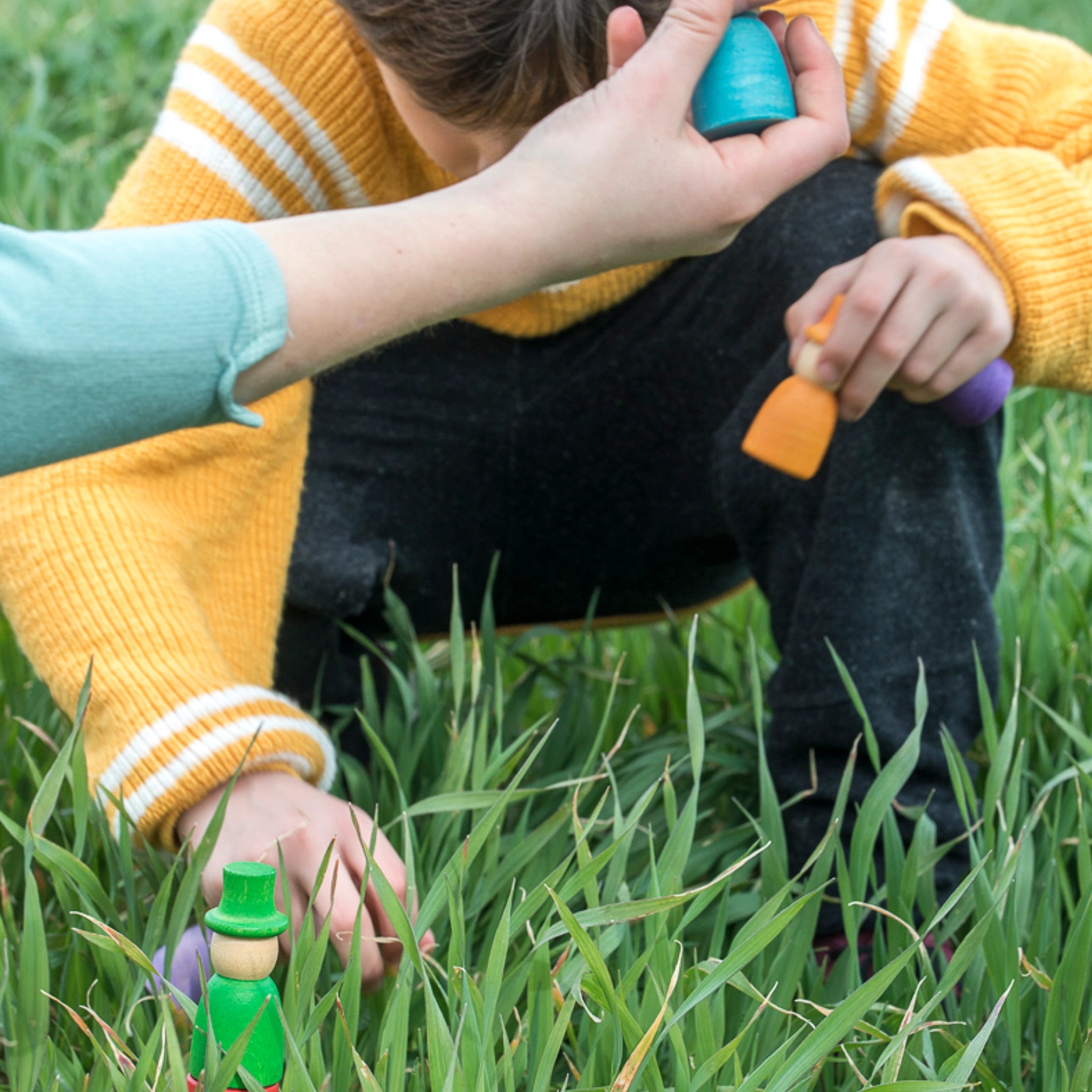 Person spielt im Gras mit Freies Spiel: Wizards, einem handgefertigten Set aus 12 bunten Holzfiguren, ideal für kreatives, freies Spiel der Kinder, hergestellt aus nachhaltig geerntetem Holz.