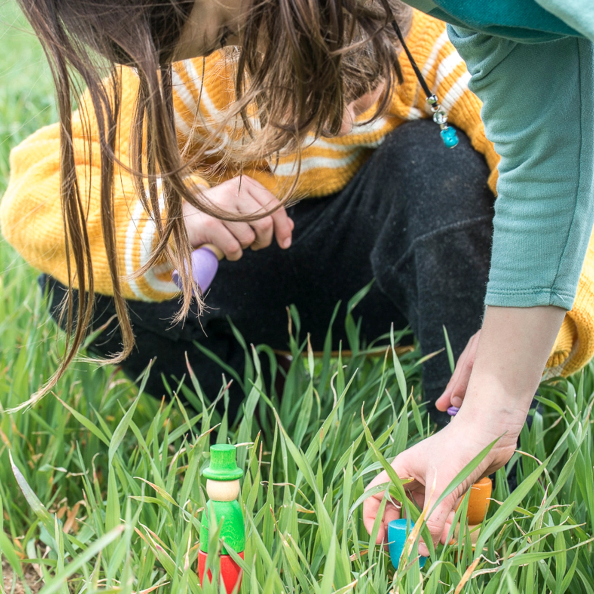 Freies Spiel: Wizards, handgefertigte Holzfiguren. Ein Junge und ein Mädchen spielen im Gras, während sie eine der bunten Regenbogen-Zaubererfiguren halten. Perfekt für kreatives, freies Spielen geeignet.