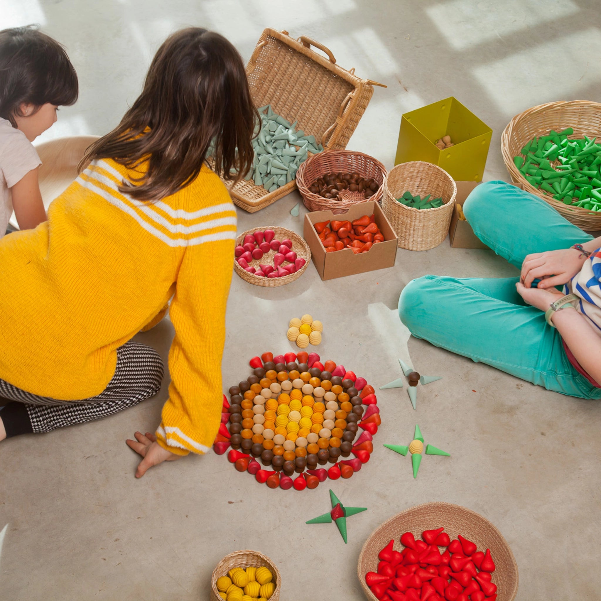 Freies Spiel: Mandala Fire-Set mit 36 handgefertigten Feuer-Elementen aus Holz, ideal für kreative Mandalas und Landschaften. Abgebildet sind Körbe voller bunter Spielobjekte, die das Set ergänzen.