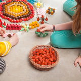 Freies Spiel: Mandala Fire – Eine Gruppe Kinder spielt mit handgefertigten, nachhaltigen Holzobjekten, die ideal für kreative Mandalas und Landschaften sind. Set enthält 36 rote Feuer-Elemente.