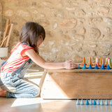 Ein Kind spielt mit dem Freies Spiel: Mandala Raindrop, einem handgefertigten Set aus 36 blauen Regentropfen aus nachhaltig geforstetem Holz, ideal für kreative Mandalas und Landschaftsgestaltungen.