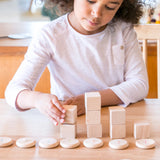 Mädchen spielt mit Freies Spiel: Coins to Count Holzbausteinen, handgefertigt in Spanien, ideal für kreatives Spiel. Enthält 60 Zählmünzen von 0 bis 9, nachhaltig hergestellt.