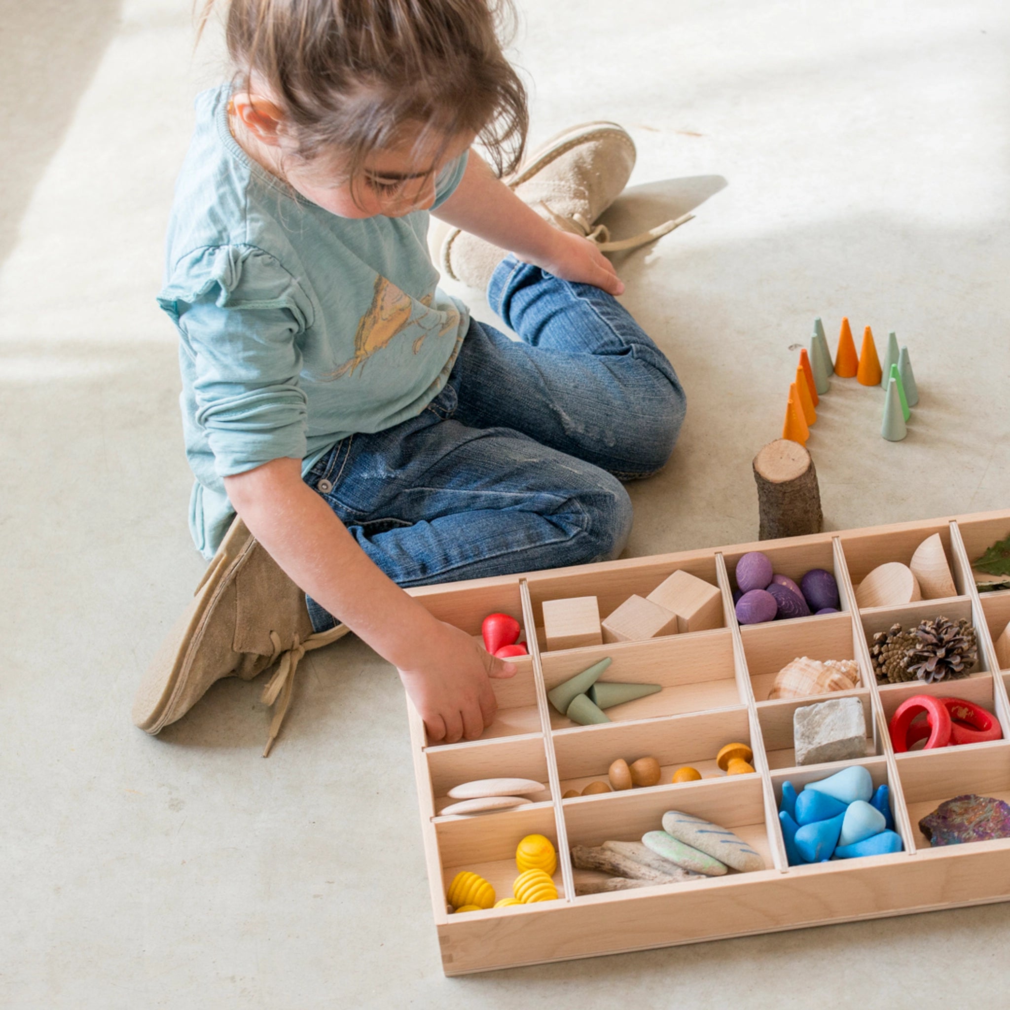 Freies Spiel: Tinker Tray – Ein Mädchen spielt mit einem handgefertigten Holz-Setzkasten, der zur Organisation von Spielzeug dient. Perfekt für kreatives Spielen, nachhaltig produziert in Spanien.