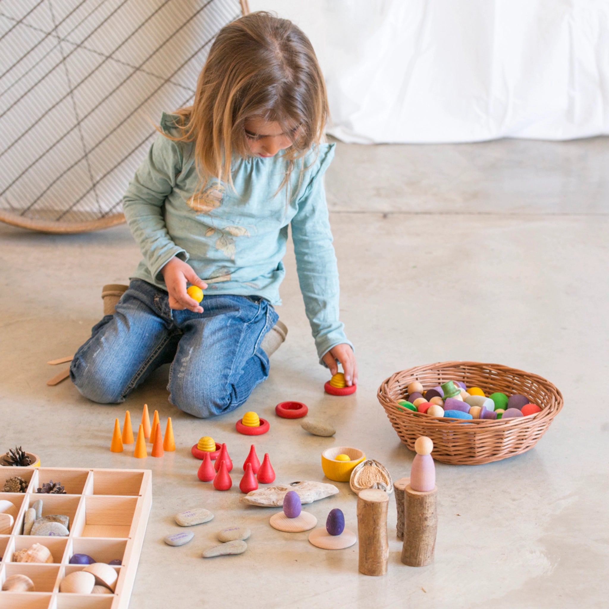 Freies Spiel: Tinker Tray aus nachhaltig geforstetem Holz, zeigt ein Mädchen beim Spielen. Enthält einen Setzkasten zur Organisation von Spielteilen, ideal für kreatives Spiel. Handgefertigt in Spanien.