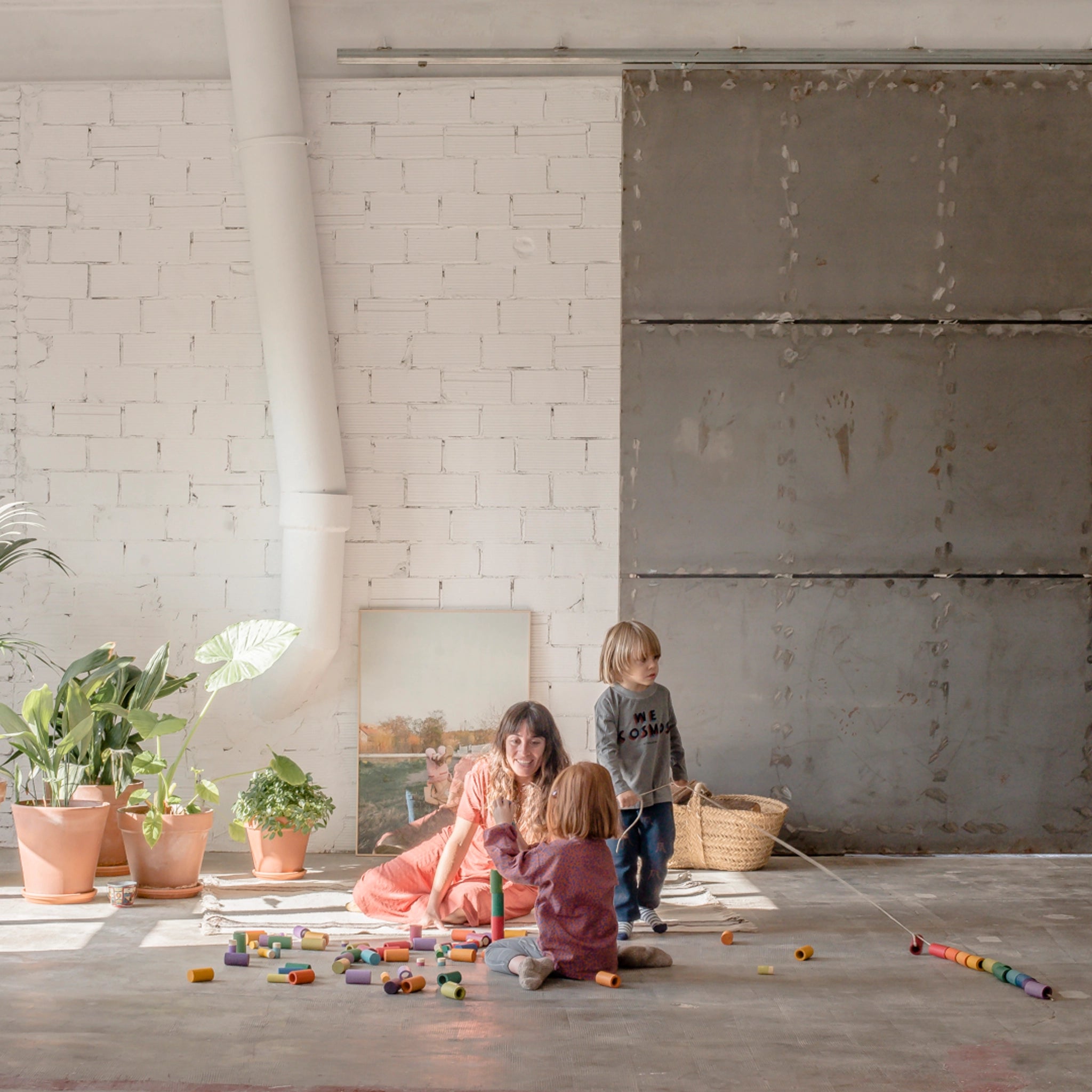 Freies Spiel: Lola, Set mit 72 handgefertigten Holzteilen, ideal für kreatives Spielen. Eine Frau und zwei Kinder spielen fröhlich mit den nachhaltig produzierten, regenbogenfarbenen Teilen auf dem Boden.