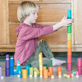 Ein Kind spielt mit den Freies Spiel: Lola, einem Set aus nachhaltig produziertem Holz mit 72 handgefertigten, regenbogenfarbenen Teilen, ideal für kreatives, freies Spiel.