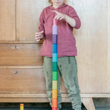 Freies Spiel: Lola - Ein Kind spielt mit einem Stapel bunter Holzbausteine, handgefertigt aus nachhaltig geforstetem Holz in Spanien, ideal für kreatives Spiel. Set mit 72 Teilen in Regenbogenfarben.