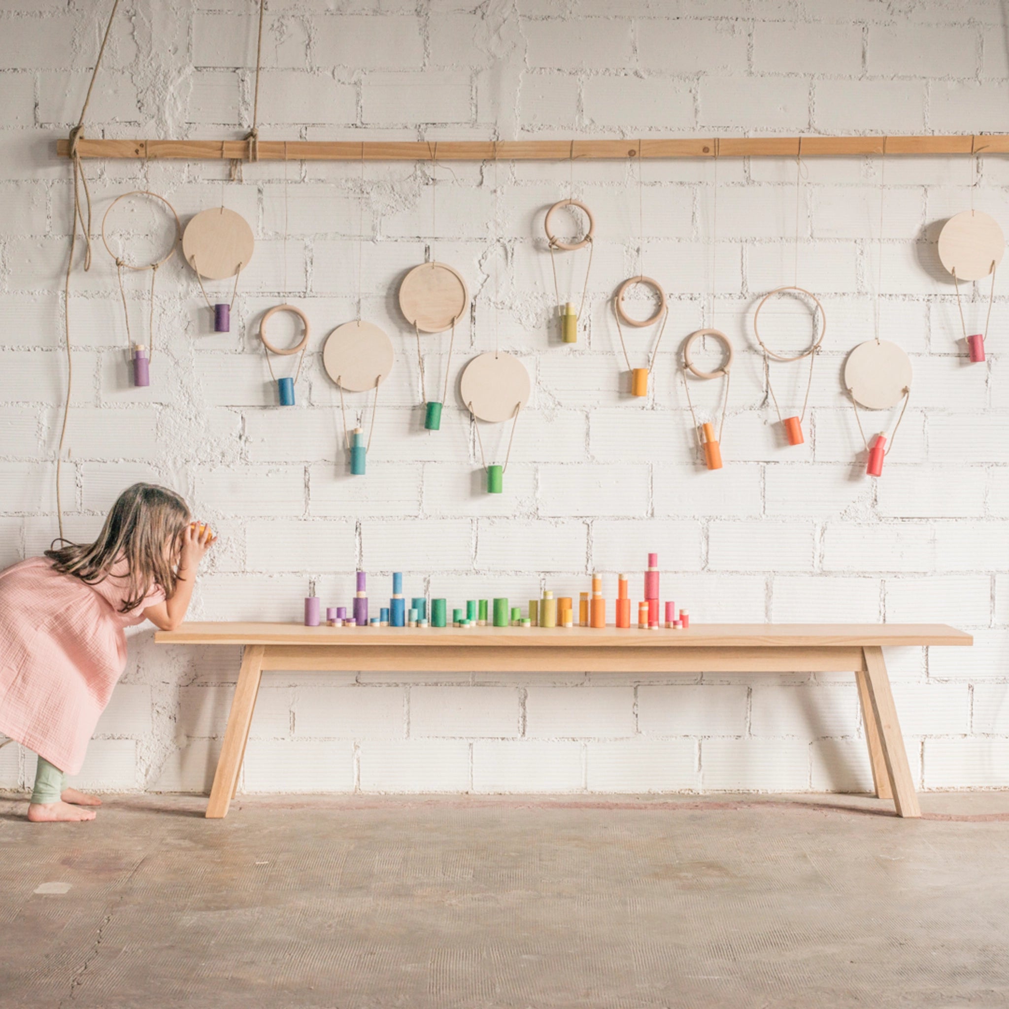 Mädchen spielt mit Freies Spiel: Lola, einem handgefertigten Set aus 72 regenbogenfarbenen Holzstücken, ideal für kreatives Spiel und nachhaltige Freude, auf einem Tisch.