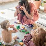 Freies Spiel: Lola-Set mit 72 handgefertigten Holzteilen, ideal für kreatives Spielen. Eine Frau und zwei Kinder spielen mit den bunten, nachhaltigen Bausteinen aus Spanien.