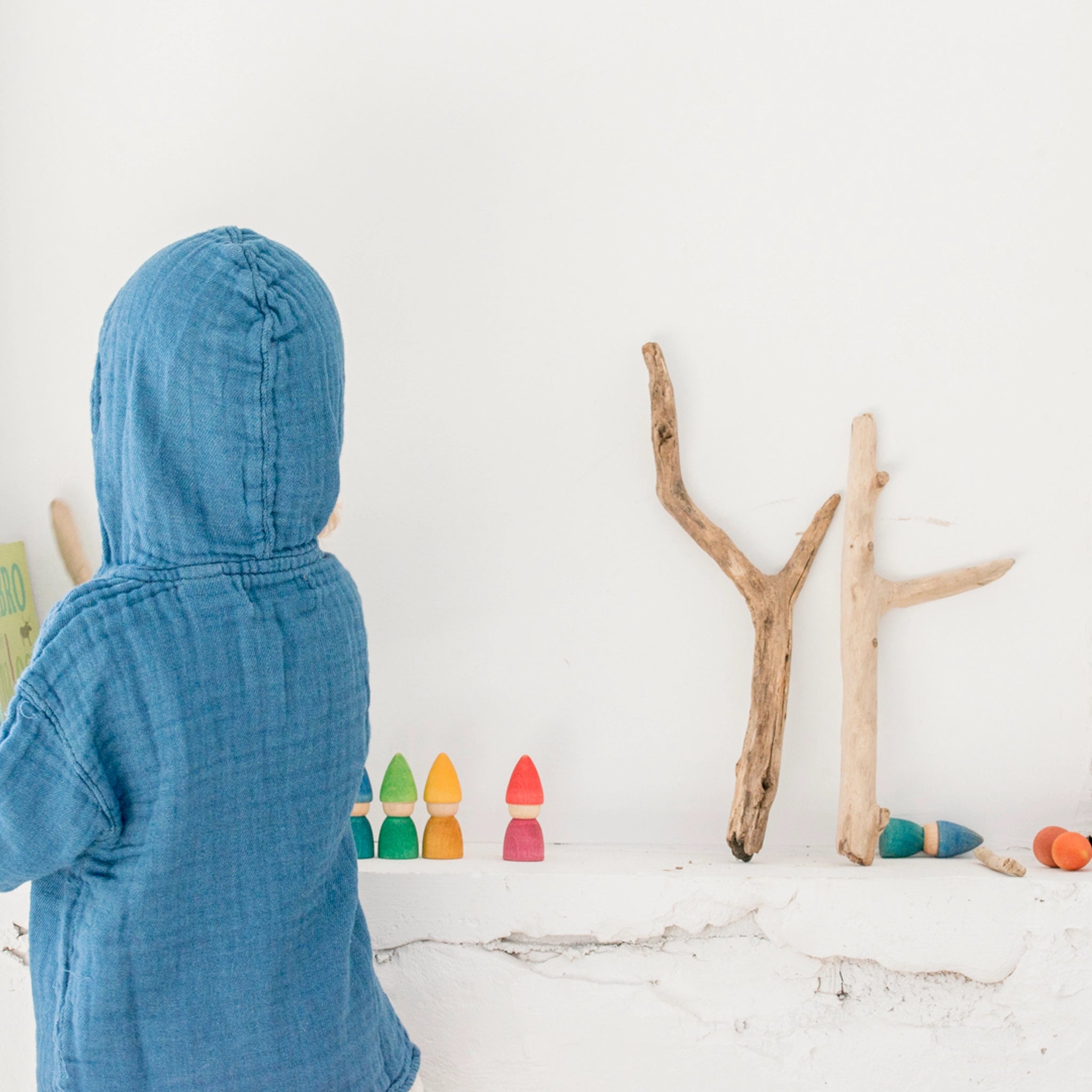 Freies Spiel: Rainbow Tomtens, ein Set aus sechs handgefertigten Zwergfiguren aus nachhaltig geforstetem Holz, ideal für kreatives Kinderspiel. Ein Kind betrachtet fasziniert die detailreichen Figuren.