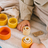 Freies Spiel: Nest Bowls aus nachhaltig geforstetem Holz, ideal für Kinder zum Bauen und Sortieren. Bild zeigt ein Kind, das mit handgefertigten Holzbechern in verschiedenen Größen und Formen spielt.