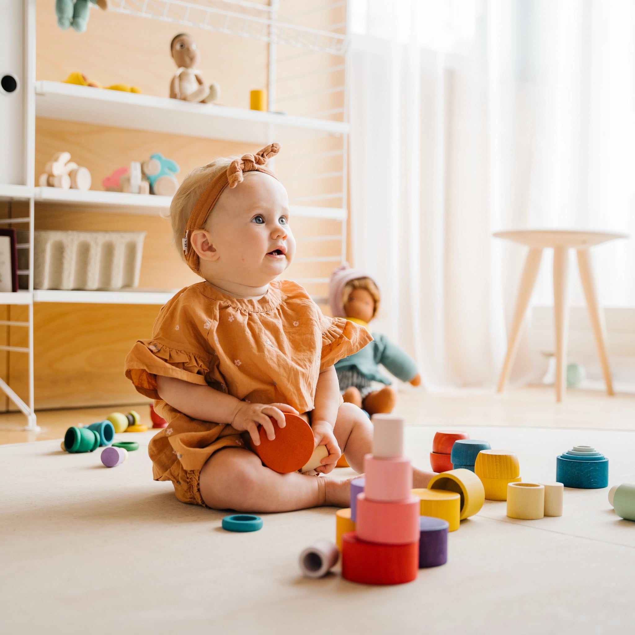 Ein Baby spielt mit Freies Spiel: Nest Bowls, einem handgefertigten Set aus 24 Holzbechern in verschiedenen Größen und Farben, ideal zum Stapeln und Sortieren.