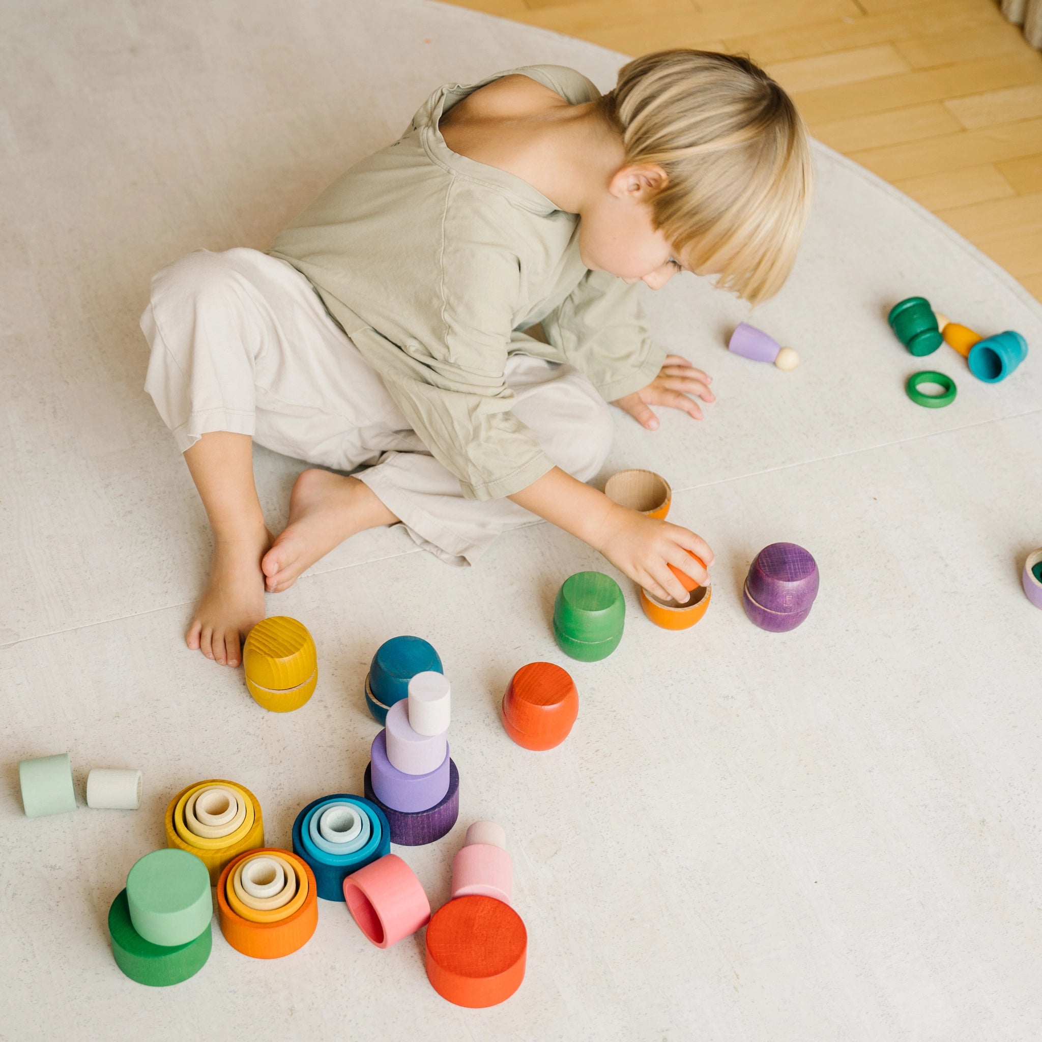 Freies Spiel: Nest Bowls – Ein Kind spielt mit handgefertigten, nachhaltigen Holzbechern zum Stapeln, Bauen und Sortieren. Das Set enthält 24 Becher in verschiedenen Größen und Farben, ideal für kreatives Spielen.