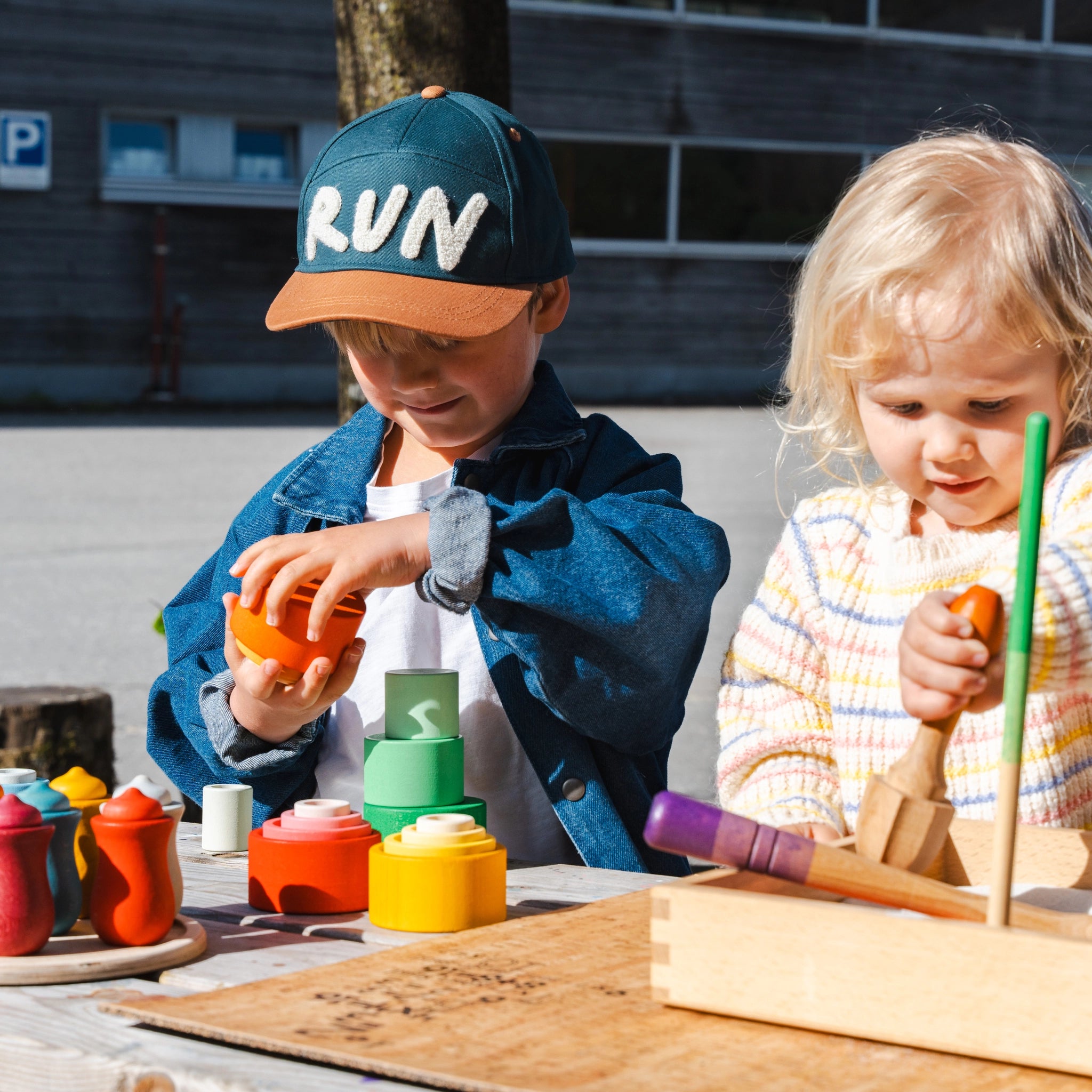 Kinder spielen mit Freies Spiel: Nest Bowls aus nachhaltig geforstetem Holz, ideal zum Bauen, Stapeln und Sortieren. Ein Junge trägt eine Mütze und spielt mit einem Holzbecher.