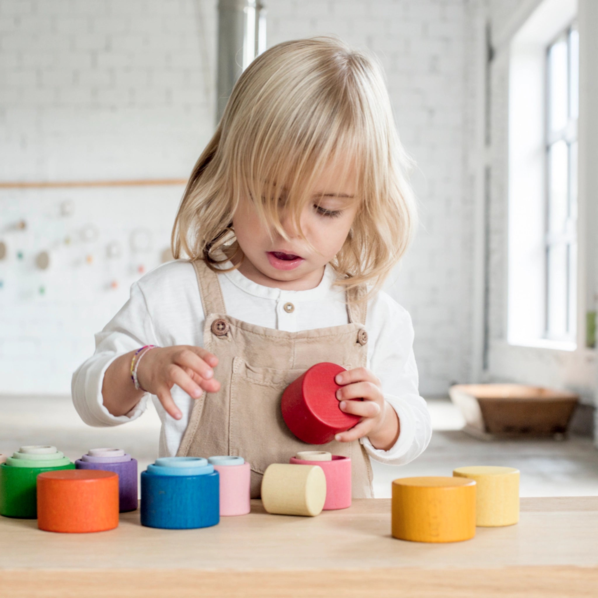 Freies Spiel: Nest Bowls aus Holz, ein Kind stapelt bunte, handgefertigte Holzbecher in verschiedenen Größen, ideal für kreatives Bauen und Sortieren.