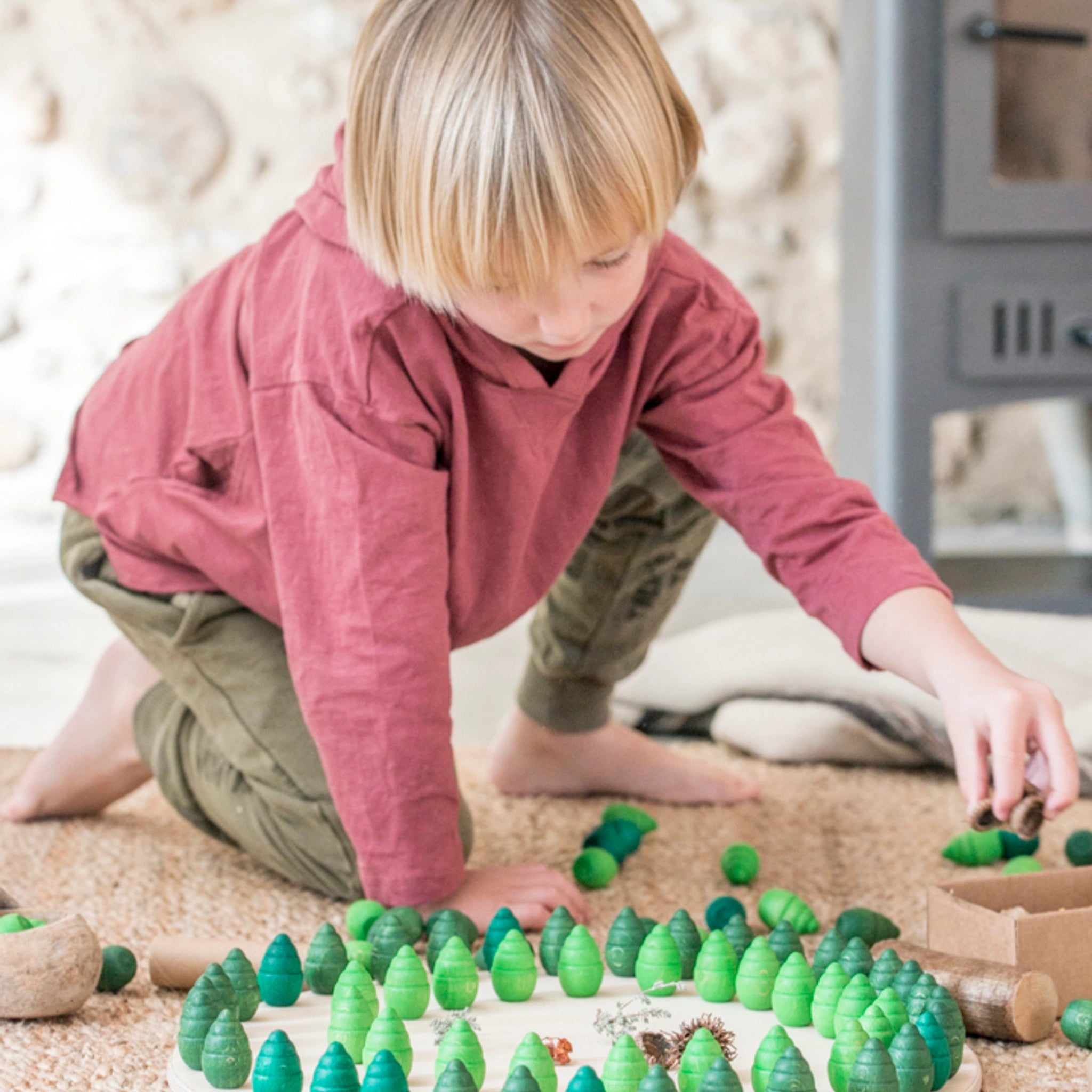 Freies Spiel: Mandala Tree - Ein Kind spielt mit handgefertigten, nachhaltig produzierten Holzspielzeugen in Form von grünen Bäumen, die ideal für kreative Mandalas und Landschaften gestaltet sind.