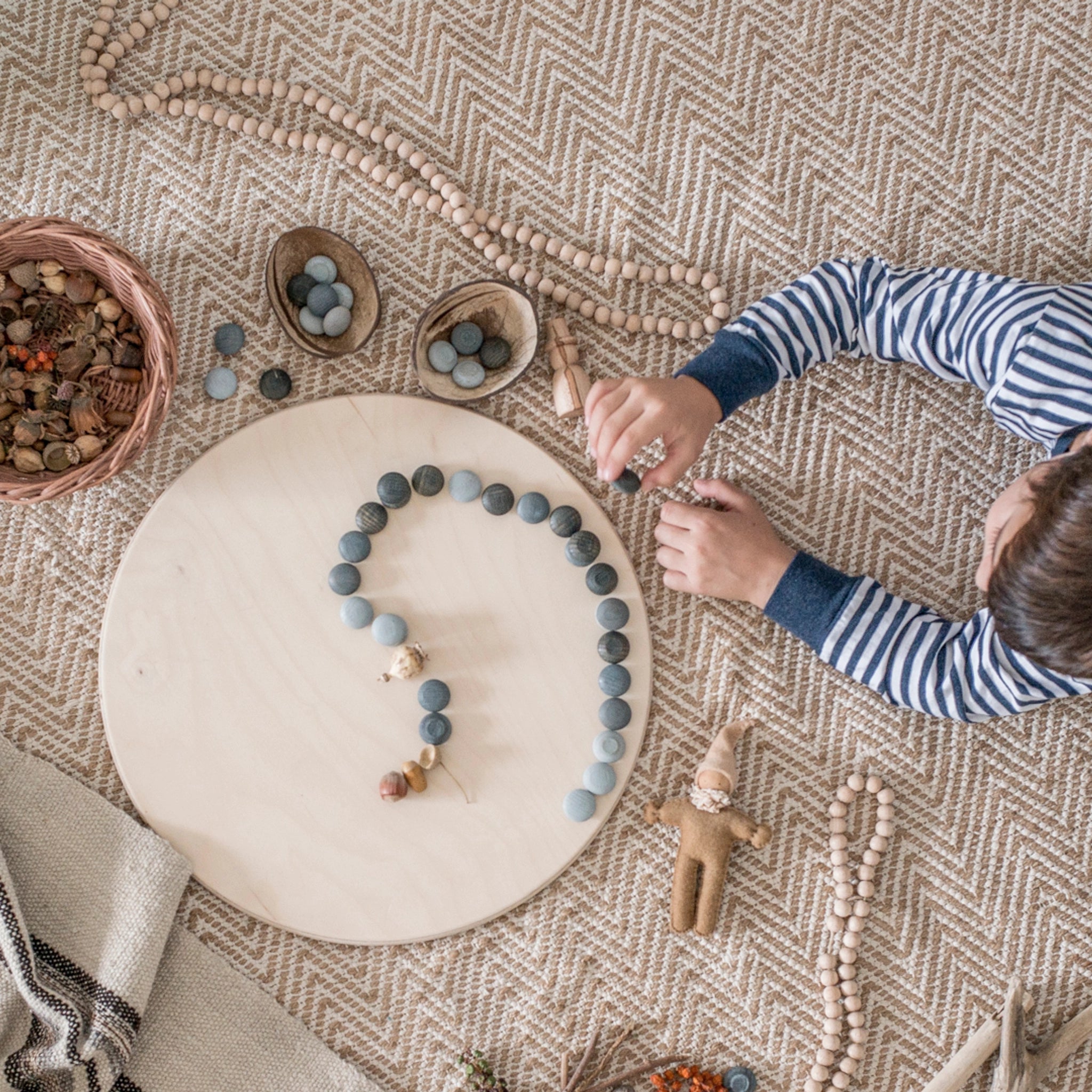 Freies Spiel: Mandala Stone, handgefertigt aus nachhaltig bewirtschaftetem Holz, ideal für kreative Kinderspiele. Im Bild spielt ein Kind mit den grauen Holzelementen, die vielseitige Kunstwerke ermöglichen.