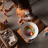 Freies Spiel: Mandala Rainbow Eggs in einer Holzschale, gehalten von einer Frau. Handgefertigt in Spanien, ideal für kreative Kinder, um bunte Mandalas zu gestalten. Perfekt für nachhaltiges, freies Spielen.