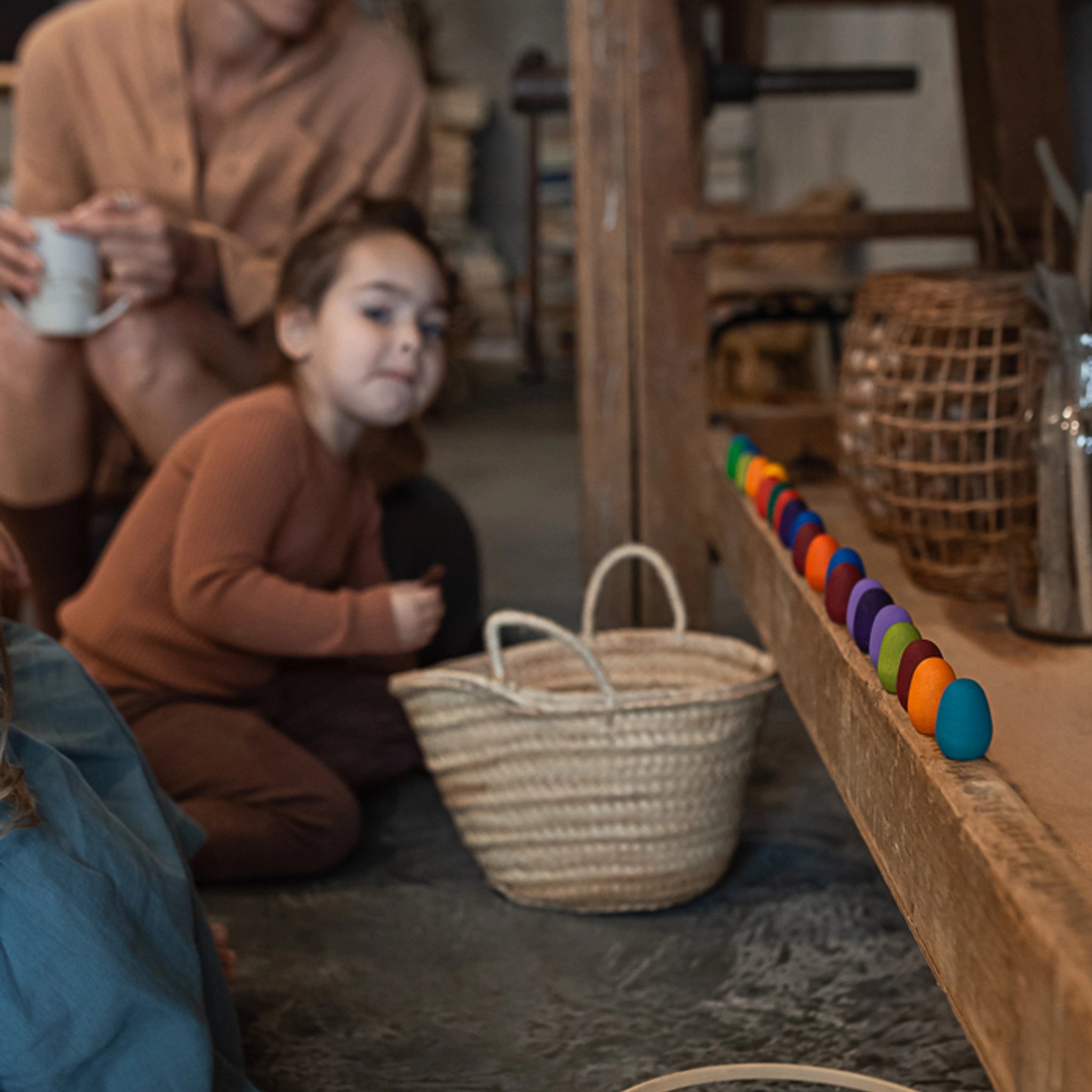 Freies Spiel: Mandala Rainbow Eggs – Eine Gruppe von Menschen sitzt am Boden mit einer Reihe handgefertigter, bunter Holzeier, ideal für kreatives Spiel und nachhaltige Kunstgestaltung.