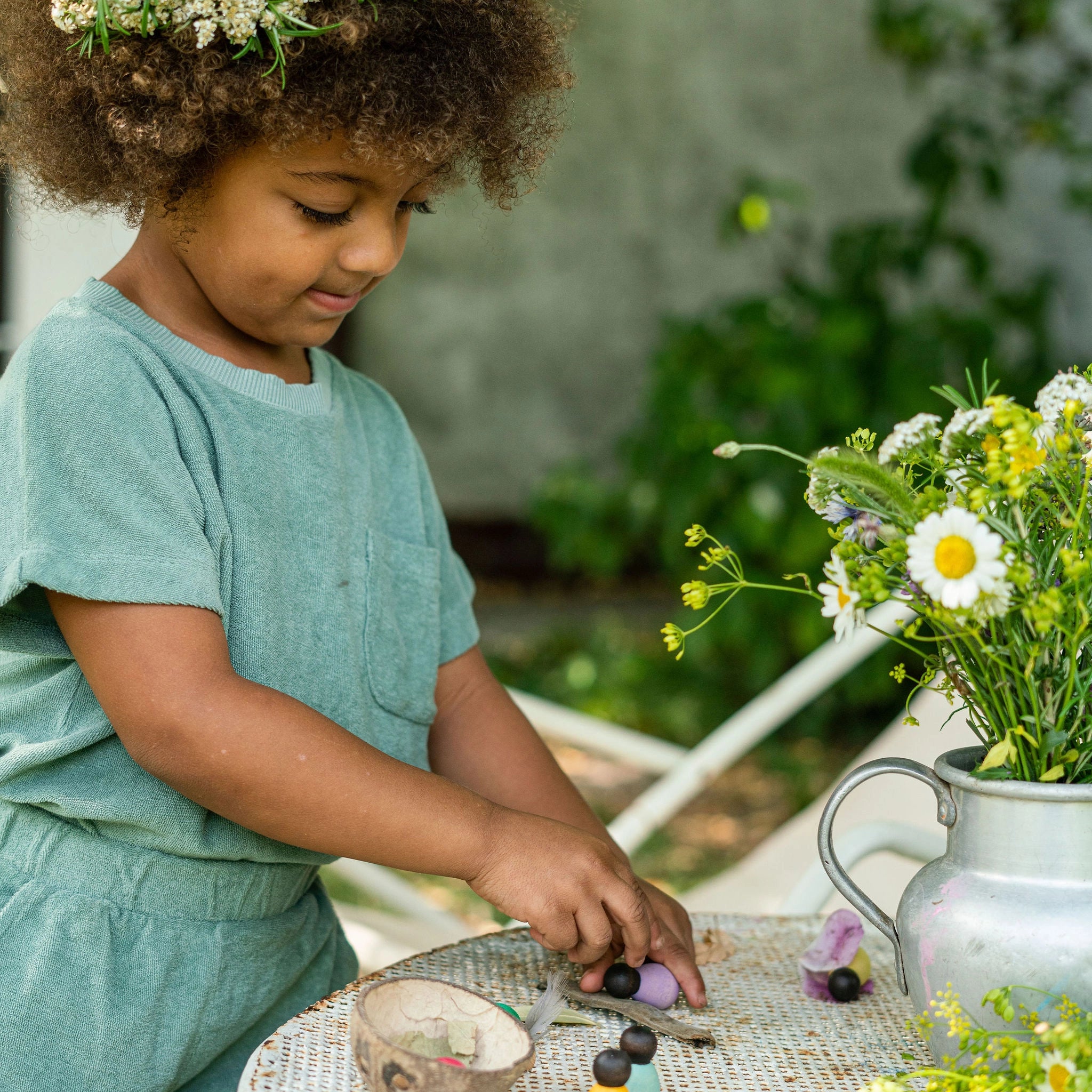 Freies Spiel: Dark Baby Nins in einer handgefertigten Kokosnussschale, ideal für kreatives Kinderspiel, präsentiert mit floralem Design und natürlichen Elementen. Nachhaltig aus Holz gefertigt.