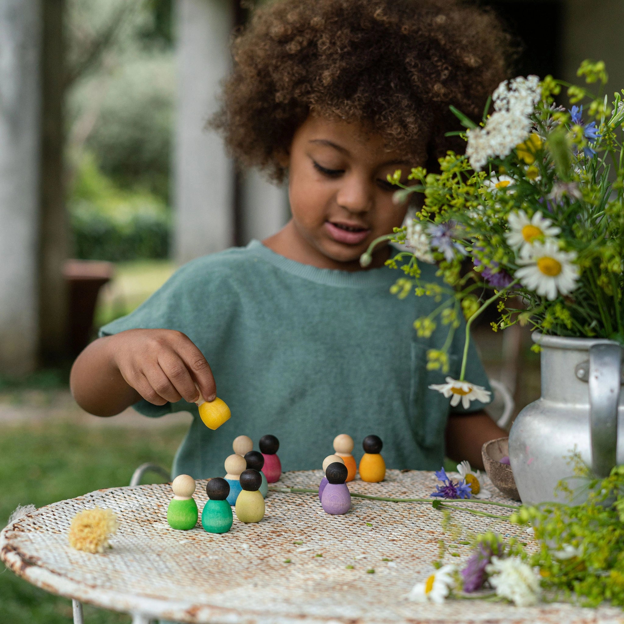 Freies Spiel: Dark Baby Nins – Ein Mädchen spielt mit handgefertigten, nachhaltigen Holzfiguren. Diese sechs Baby Nins-Figuren sind in einer Kokosnussschale präsentiert, ideal für kreatives Kinderspiel.