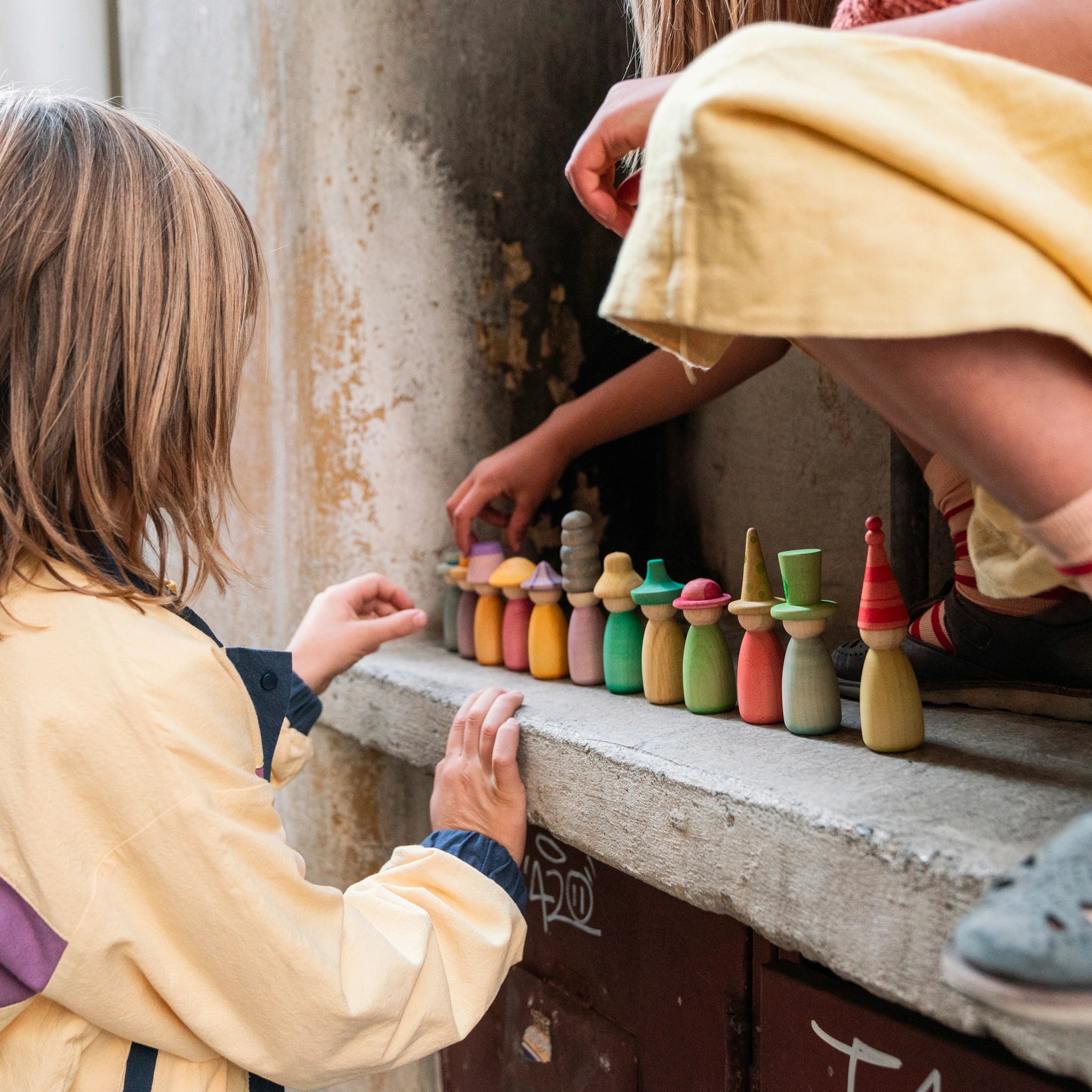 Freies Spiel: Fancy Nins, handgefertigte Holzfiguren aus Spanien, zeigen Kinder, die mit bunten Figuren spielen, ideal für kreatives Spiel. Nachhaltig produziert, fördern sie Freude und soziale Fairness.