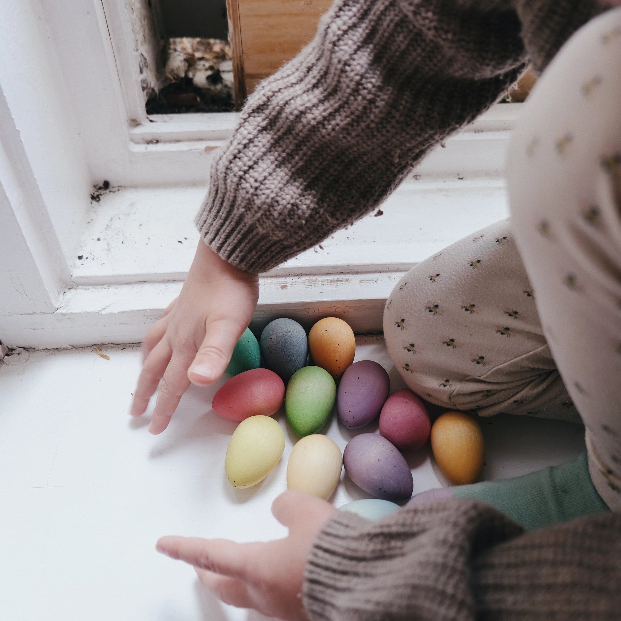 Kind berührt bunte Freies Spiel: Happy Eggs aus nachhaltig geforstetem Holz, handbemalt, ideal für kreatives Spiel. Handgefertigt in Spanien, symbolisieren sie KLICKKLACKs nachhaltige und ästhetische Produktphilosophie.