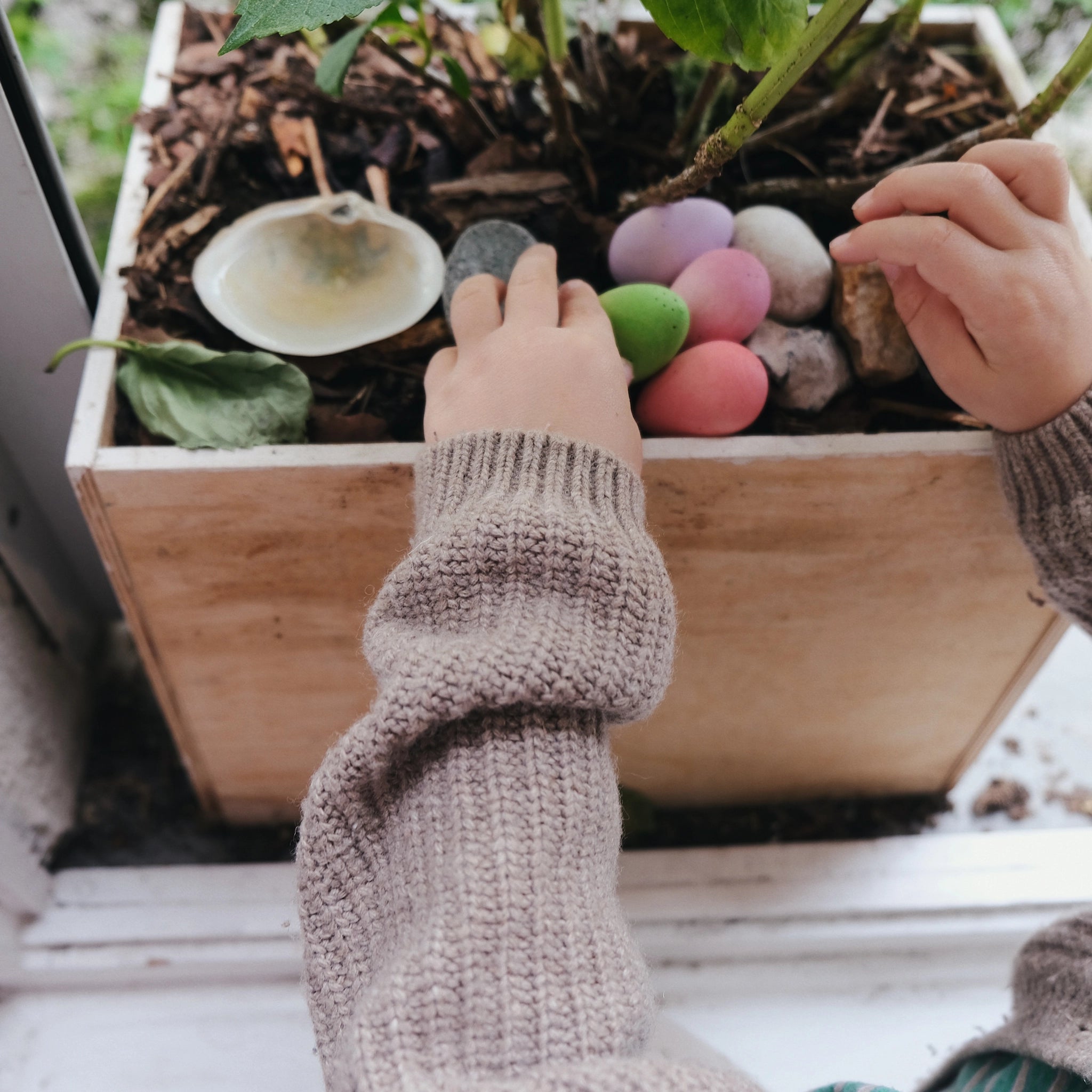 Freies Spiel: Happy Eggs – Hand hält bunte Eier mit handgemalten Punkten, umgeben von Pflanzen und Steinen. Handgefertigt aus nachhaltigem Holz, fördert kreatives Spielen und soziale Fairness.