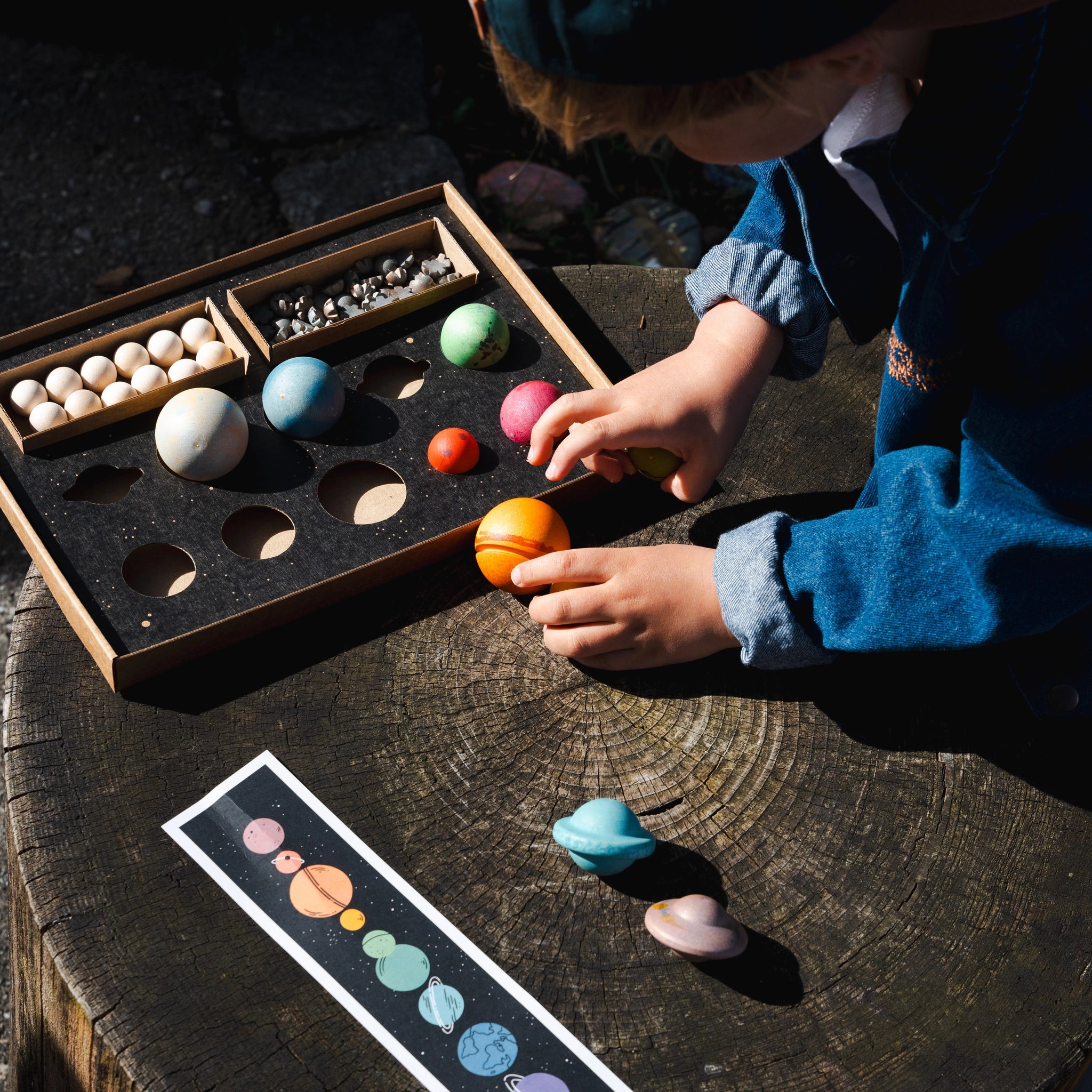 Freies Spiel: Dear Universe Holzset, zeigt ein Kind, das mit 40 handgefertigten Himmelskörpern spielt. Nachhaltig geforstetes Holz, ideal für kreatives Spiel drinnen und draußen.