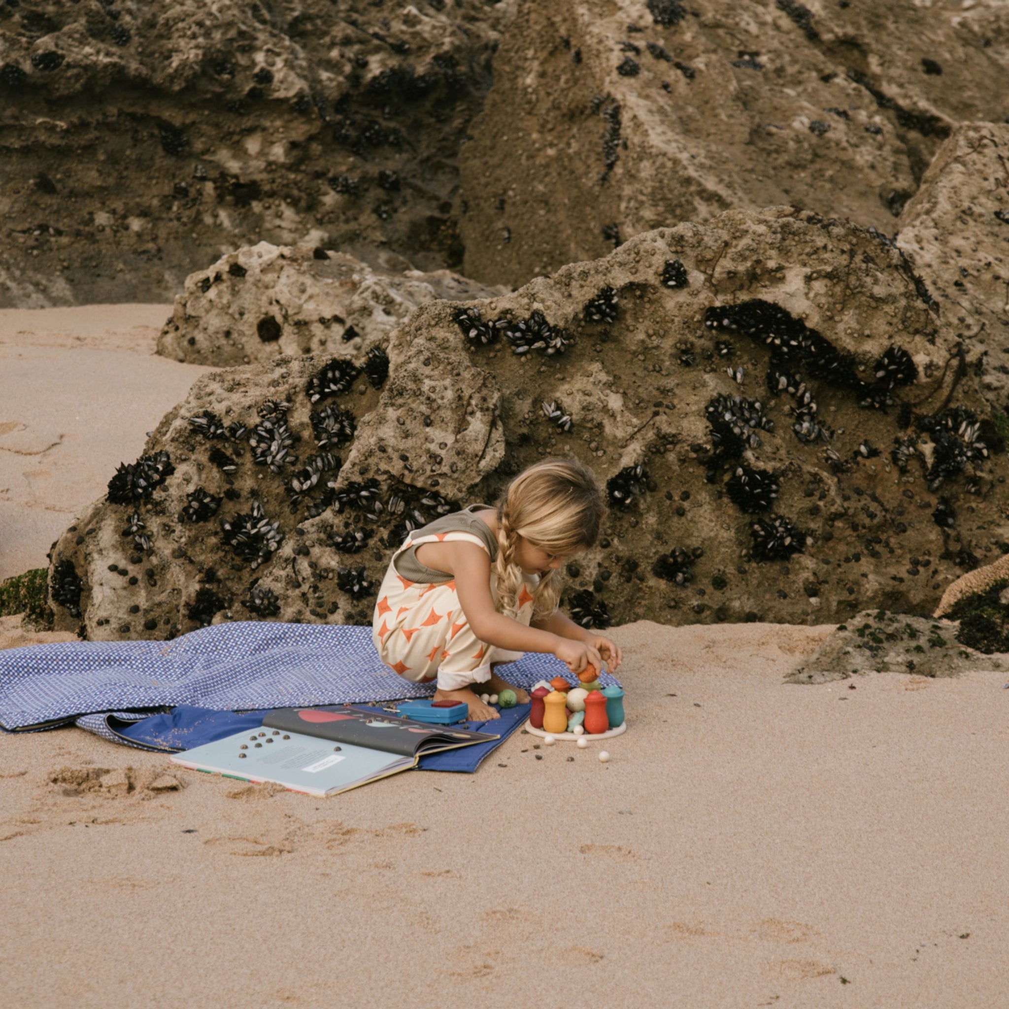 Mädchen spielt am Strand mit dem Holzspielset Freies Spiel: Dear Universe, bestehend aus 40 handgefertigten Himmelskörpern, ideal für kreatives Spiel drinnen und draußen, aus nachhaltiger Produktion.