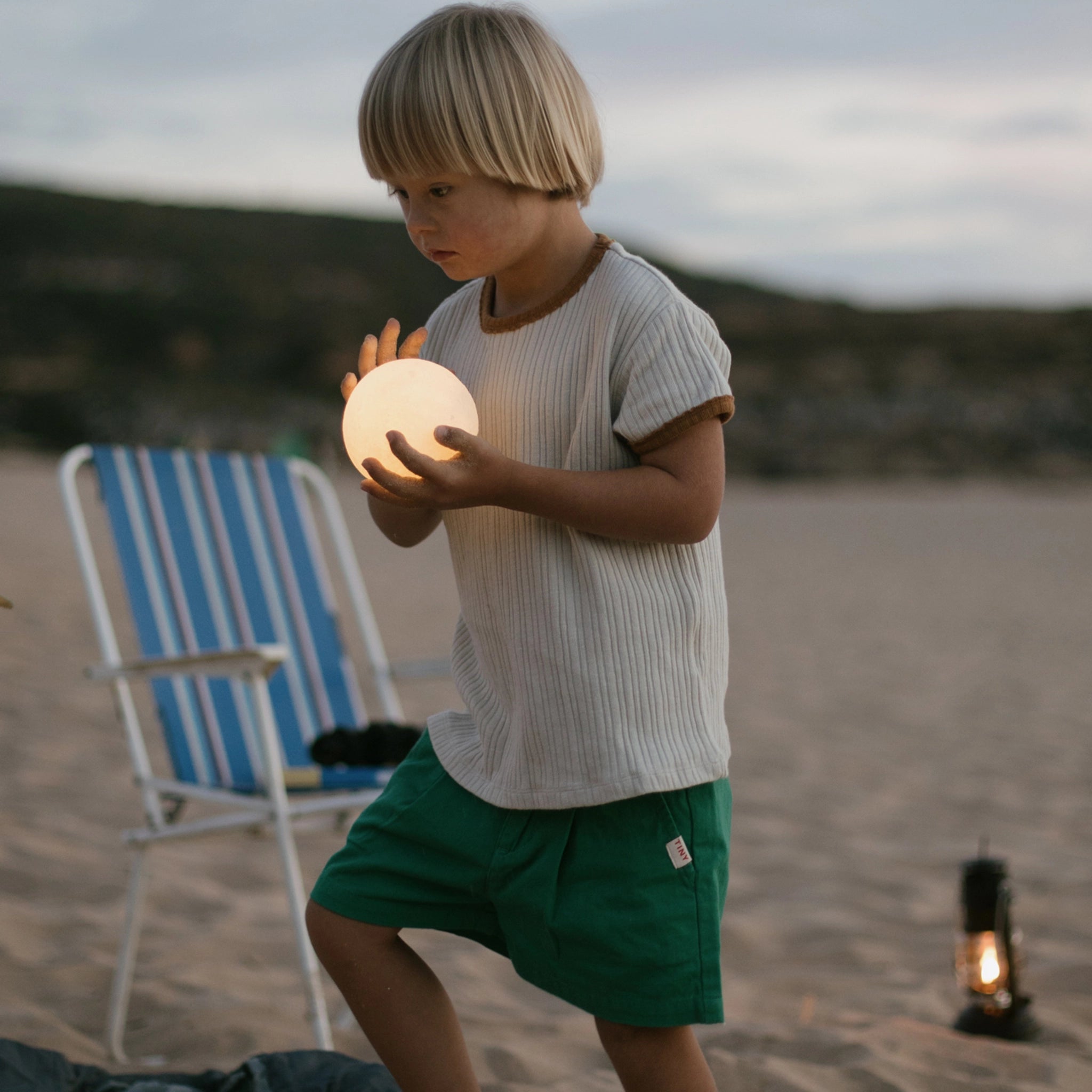 Kind hält leuchtenden Ball am Strand, symbolisiert Freies Spiel: Dear Universe. Das Set besteht aus 40 handgefertigten, hölzernen Himmelskörpern, ideal für kreatives Spiel drinnen und draußen.