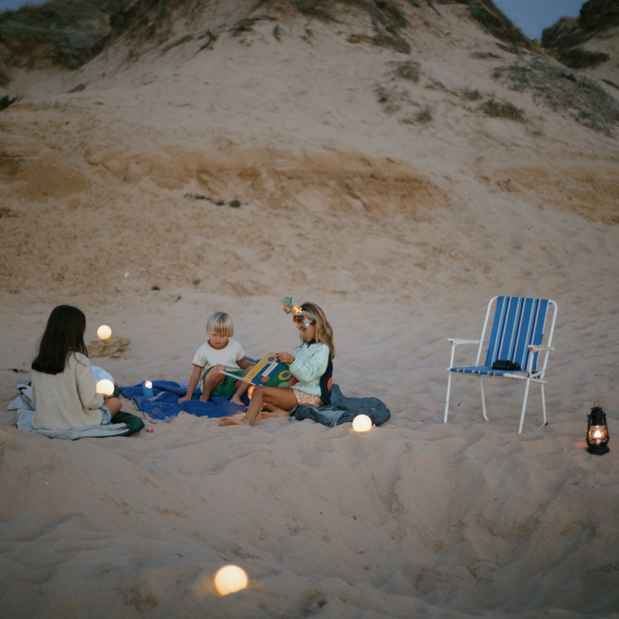 Freies Spiel: Dear Universe – Menschen auf einer Decke am Strand, umgeben von handgefertigten, hölzernen Himmelskörpern. Perfekt für kreatives, nachhaltiges Spiel, drinnen und draußen.