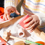 Freies Spiel: Tools – Ein Kind spielt mit Sand, während Hände Sand in eine Box gießen. Handgefertigte Holzinstrumente, ideal für kreatives Spielen drinnen und draußen, aus nachhaltigem Holz gefertigt.