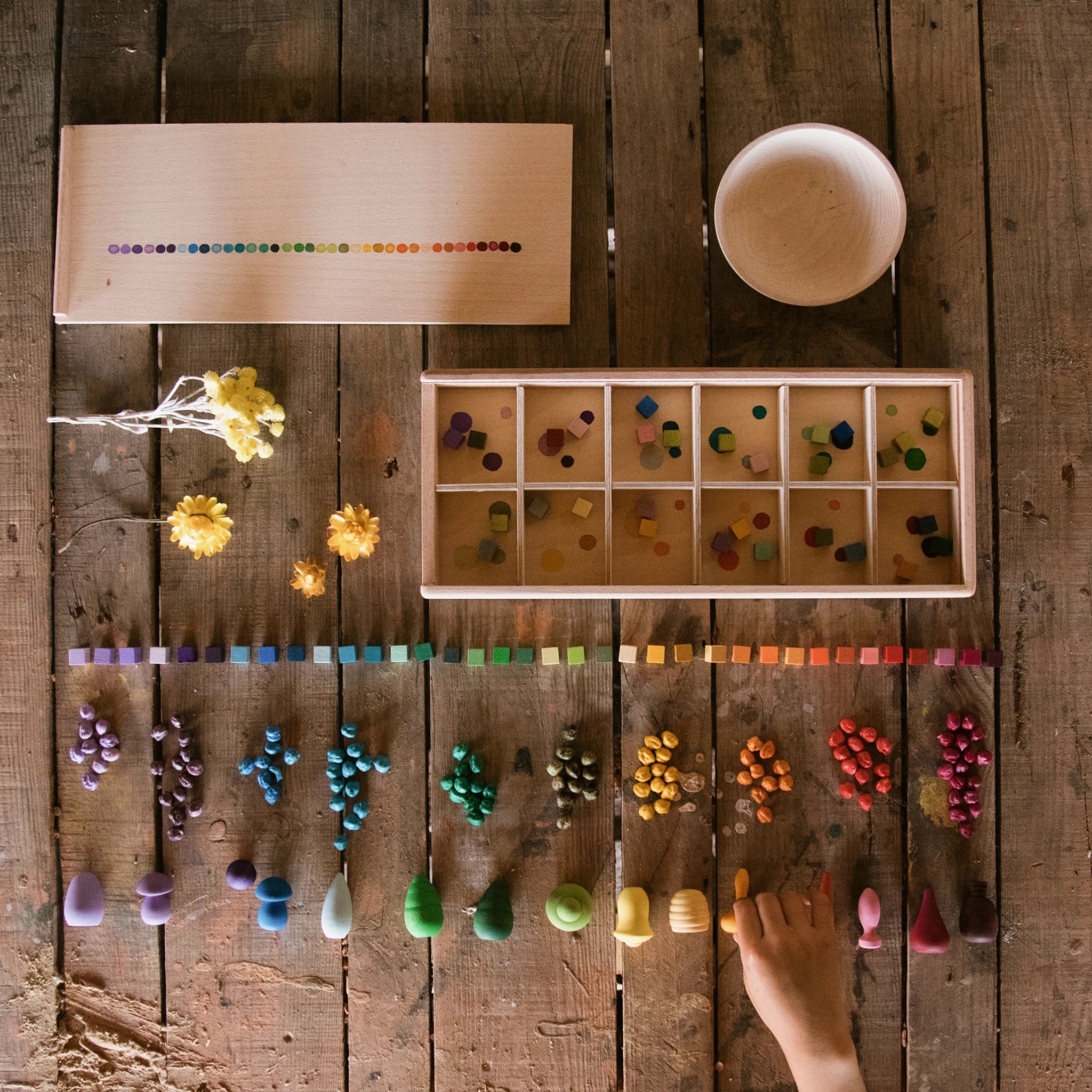 Freies Spiel: Mis and Match – Ein handgefertigter Setzkasten aus nachhaltig geforstetem Holz, gefüllt mit über 400 bunten Holzwürfeln, ideal für kreatives Spiel. Eine Hand berührt die Box.