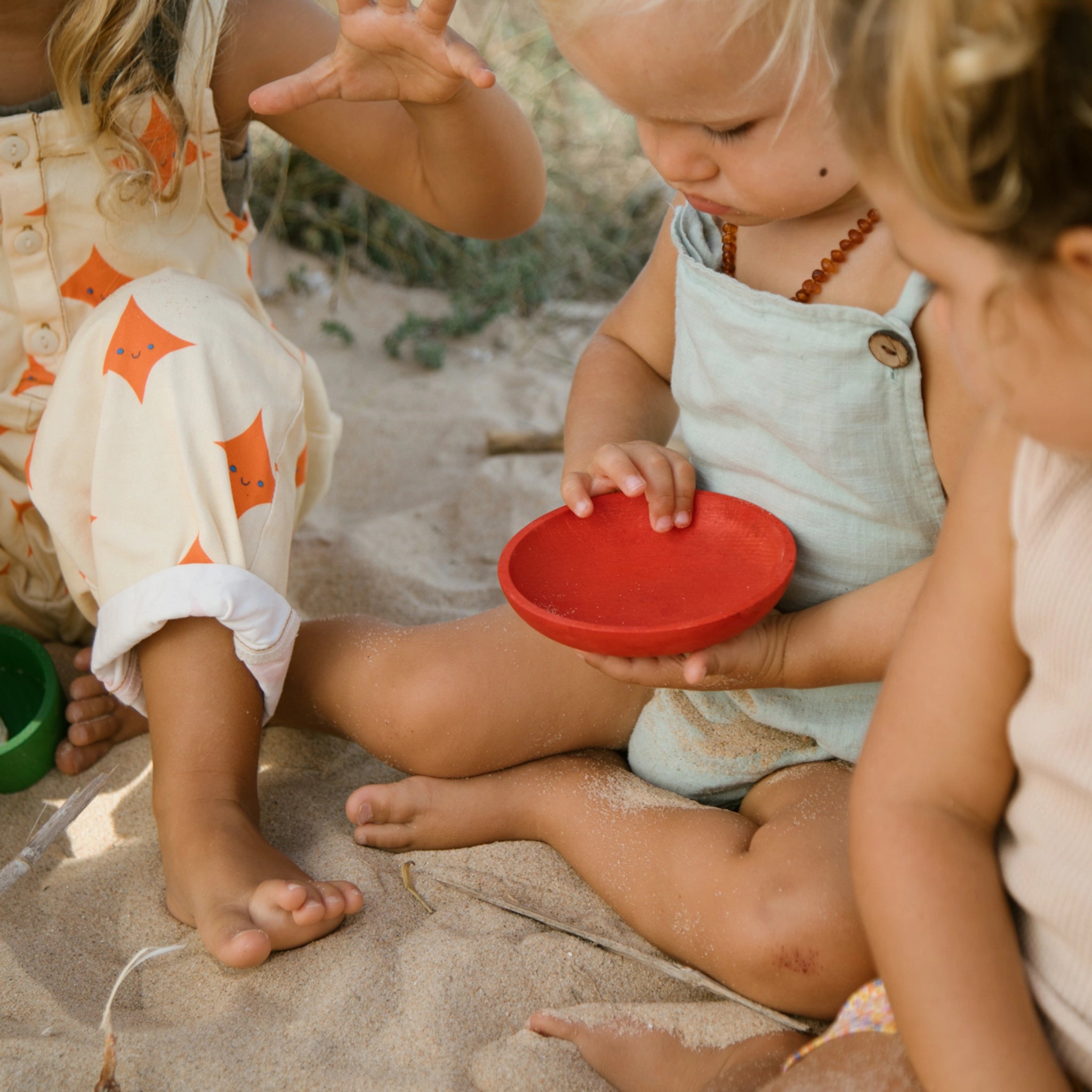 Kinder spielen im Sand, während sie mit dem Produkt Freies Spiel: Pots interagieren, einem Set aus sechs handgefertigten, bunten Holztöpfchen, ideal für kreatives Spiel drinnen und draußen.