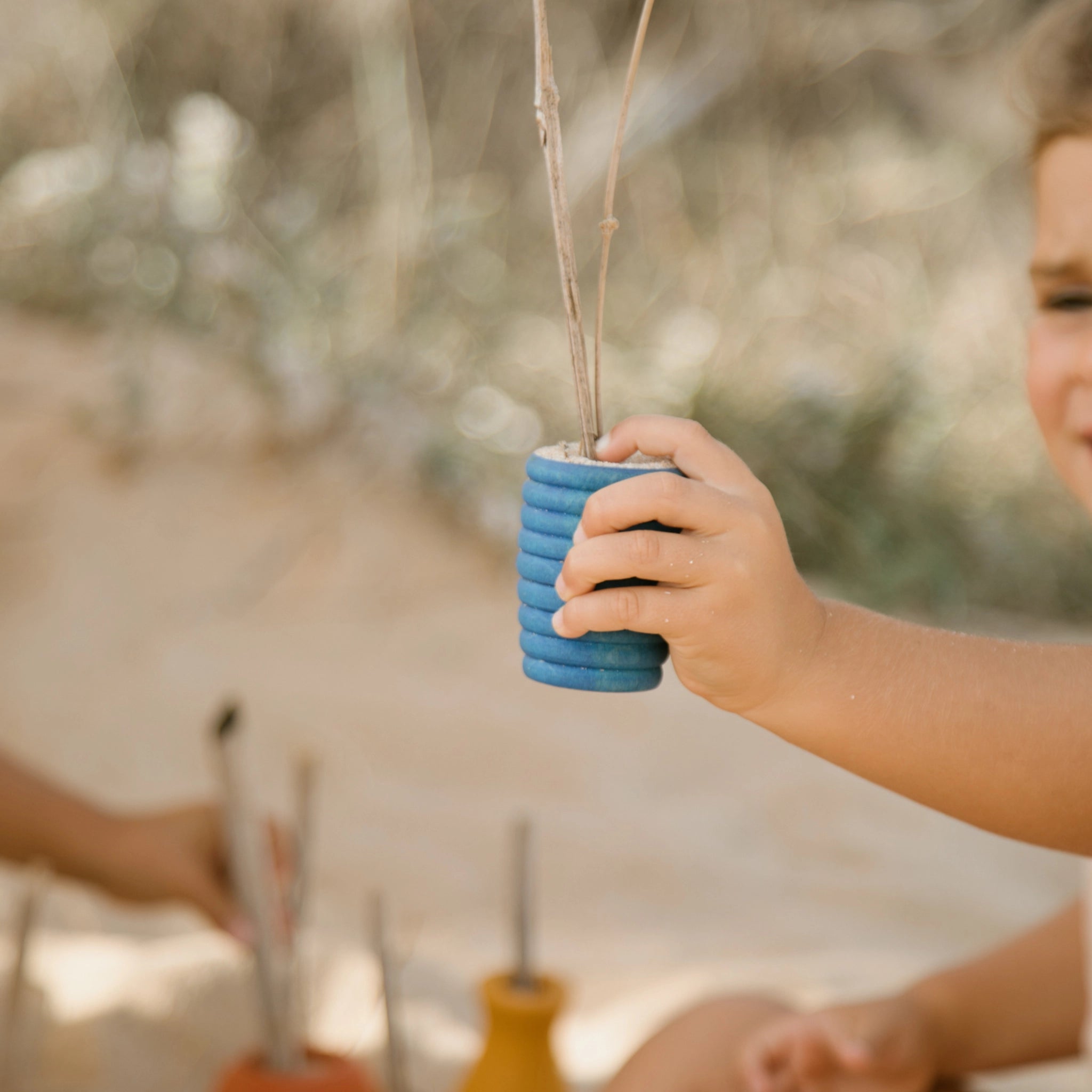 Kind hält Freies Spiel: Pots, ein Set aus 6 handgefertigten Holztöpfchen, ideal für freies Spiel drinnen und draußen. Nachhaltig produziert in Spanien, unterstützt es ästhetisch-modernes Design.