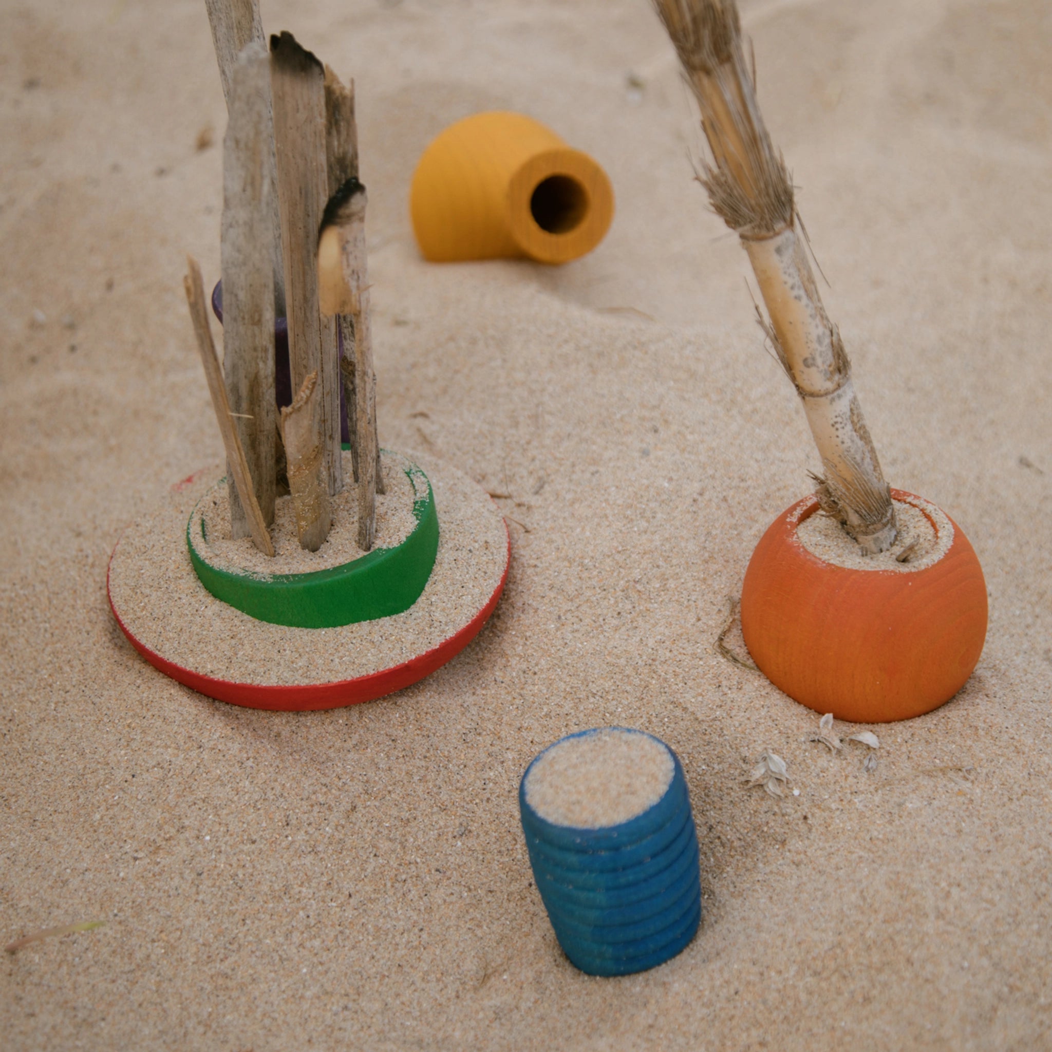 Freies Spiel: Pots aus nachhaltig geforstetem Holz, handgefertigt in Spanien. Sechs bunte Töpfchen, ideal für kreatives Spielen, abgebildet auf Sand mit Holzstäbchen und Pflanzen im Hintergrund.