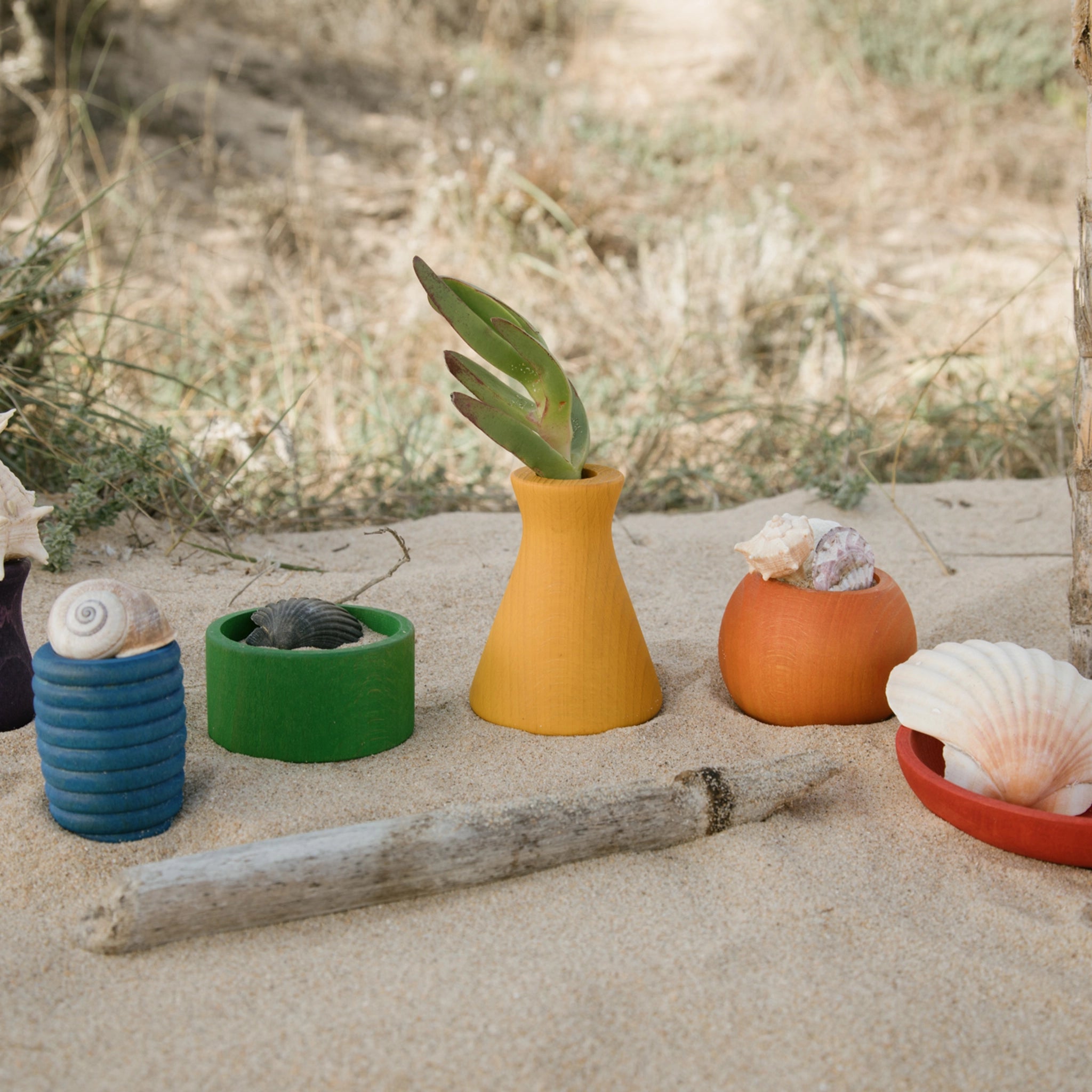 Freies Spiel: Pots aus nachhaltigem Holz, ein Set aus sechs handgefertigten, bunten Töpfchen, präsentiert auf Sand. Ideal für kreatives Spiel und hergestellt in Spanien.